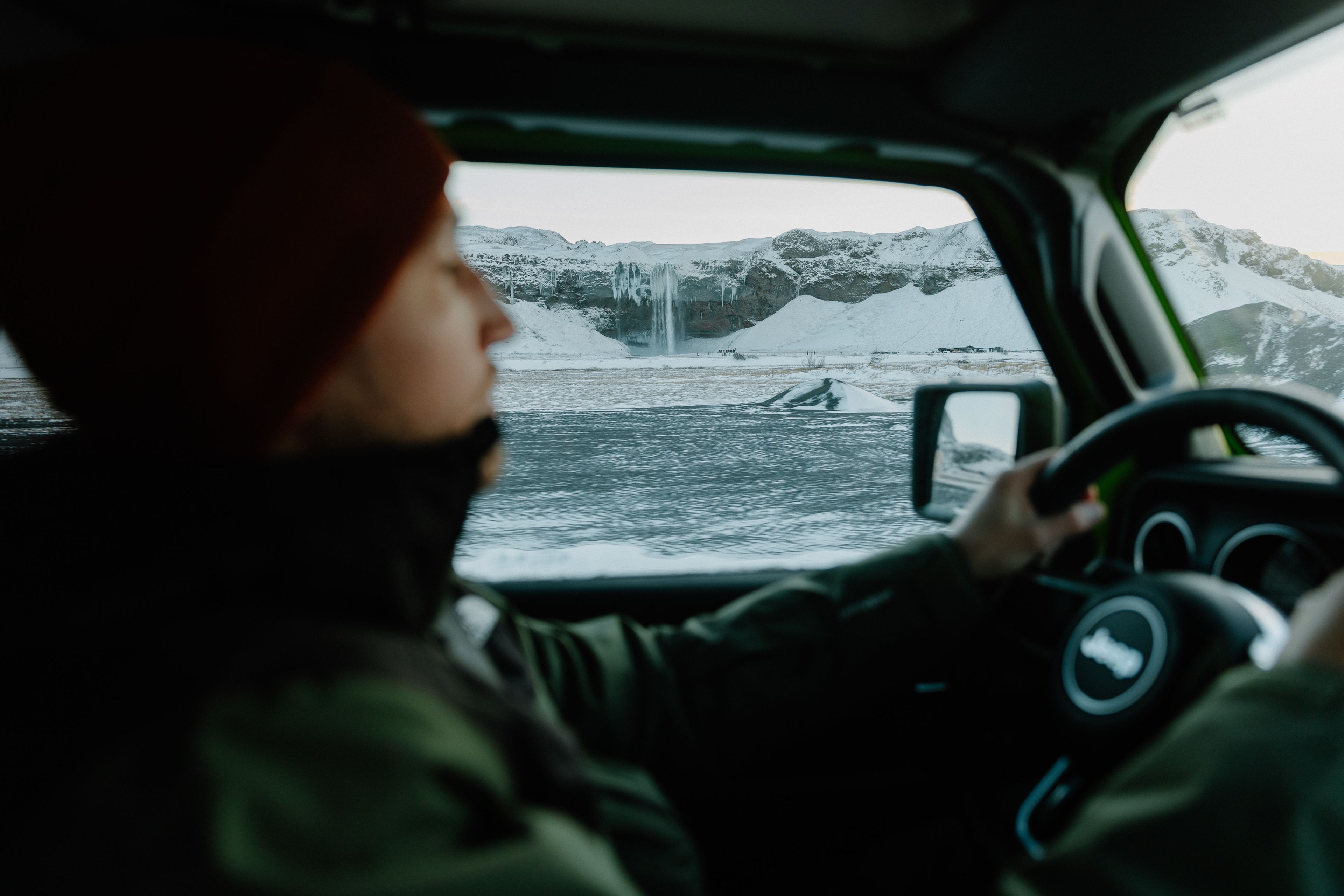 a person driving a 4x4 Jeep Wrangler rental car in Iceland near a waterfall