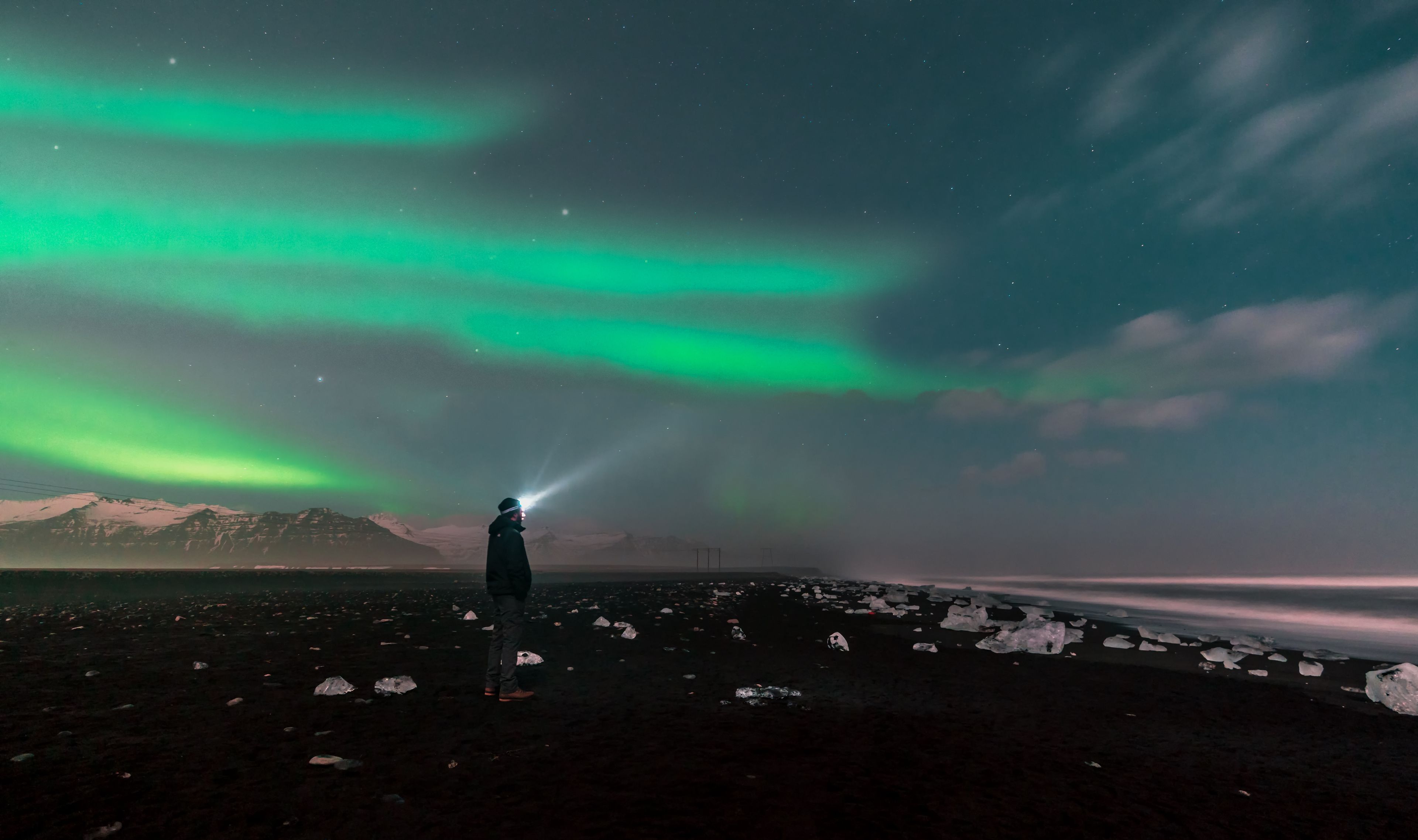man observing with his headlamp the northern lights of Iceland, on the beautiful diamond beach 