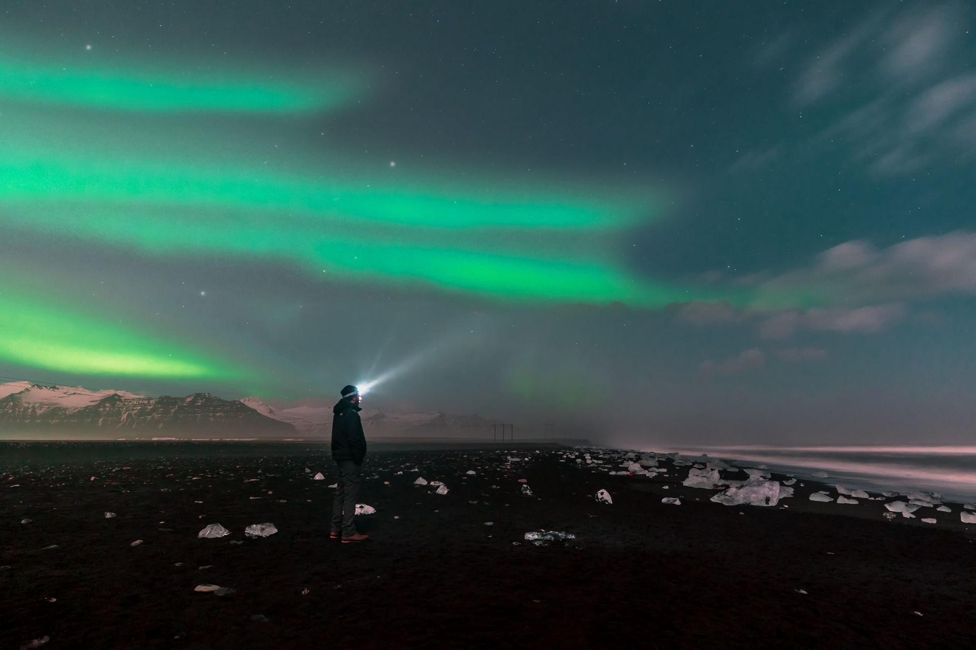 man observing with his headlamp the northern lights of Iceland, on the beautiful diamond beach 