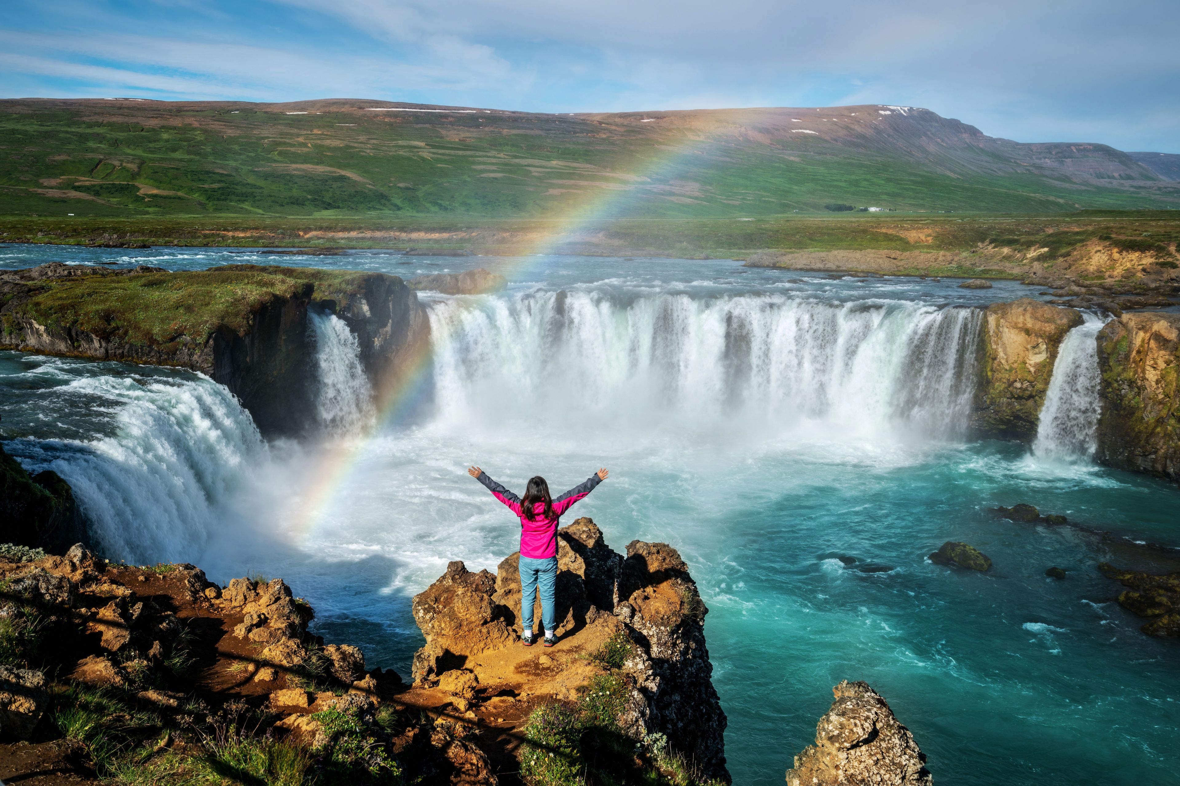A girl in front of the Goðafoss waterfall and a beautiful rainbow