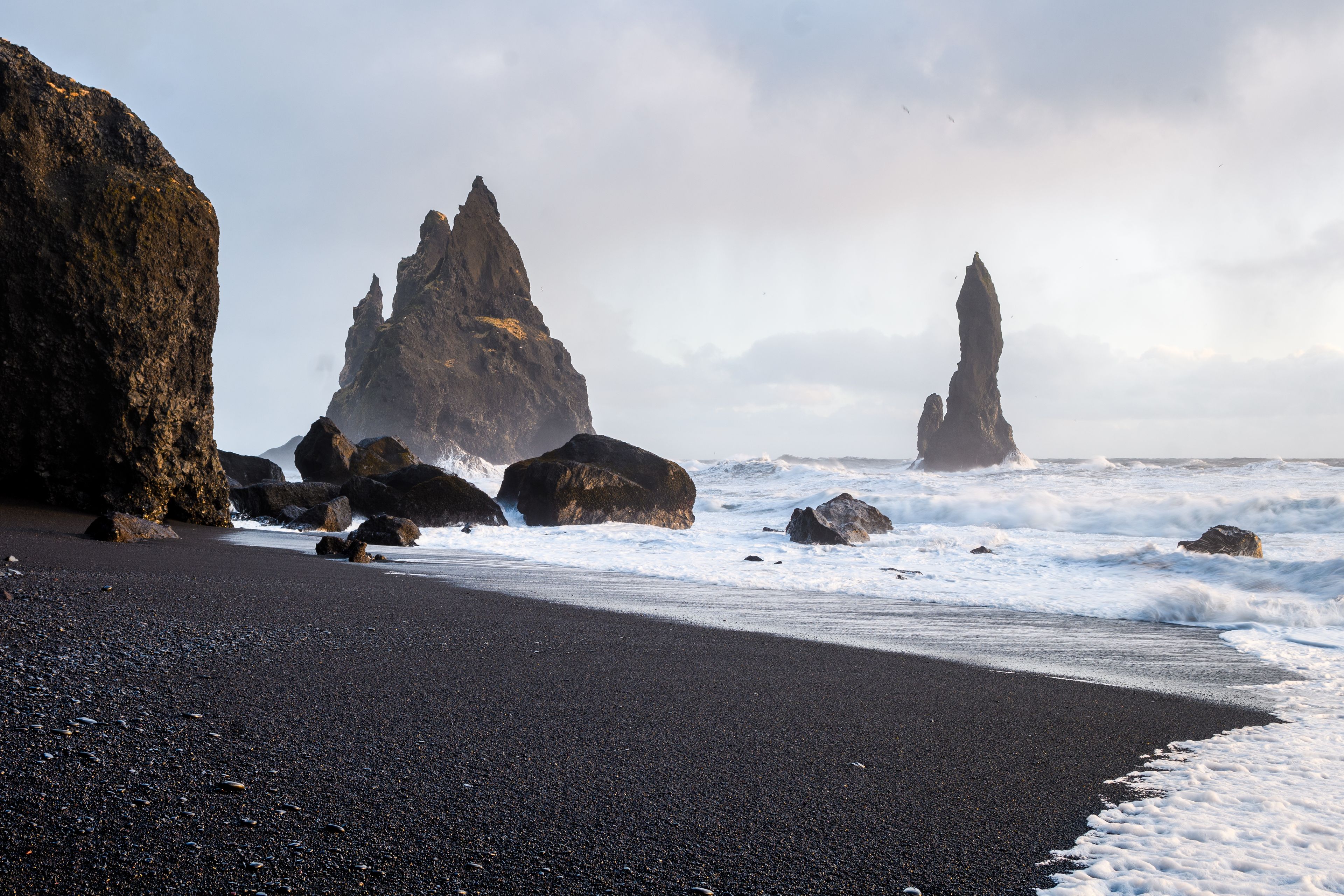 sneaker waves on reynisfjara black sand beach on iceland's south coast with black volcanic rock on the left side