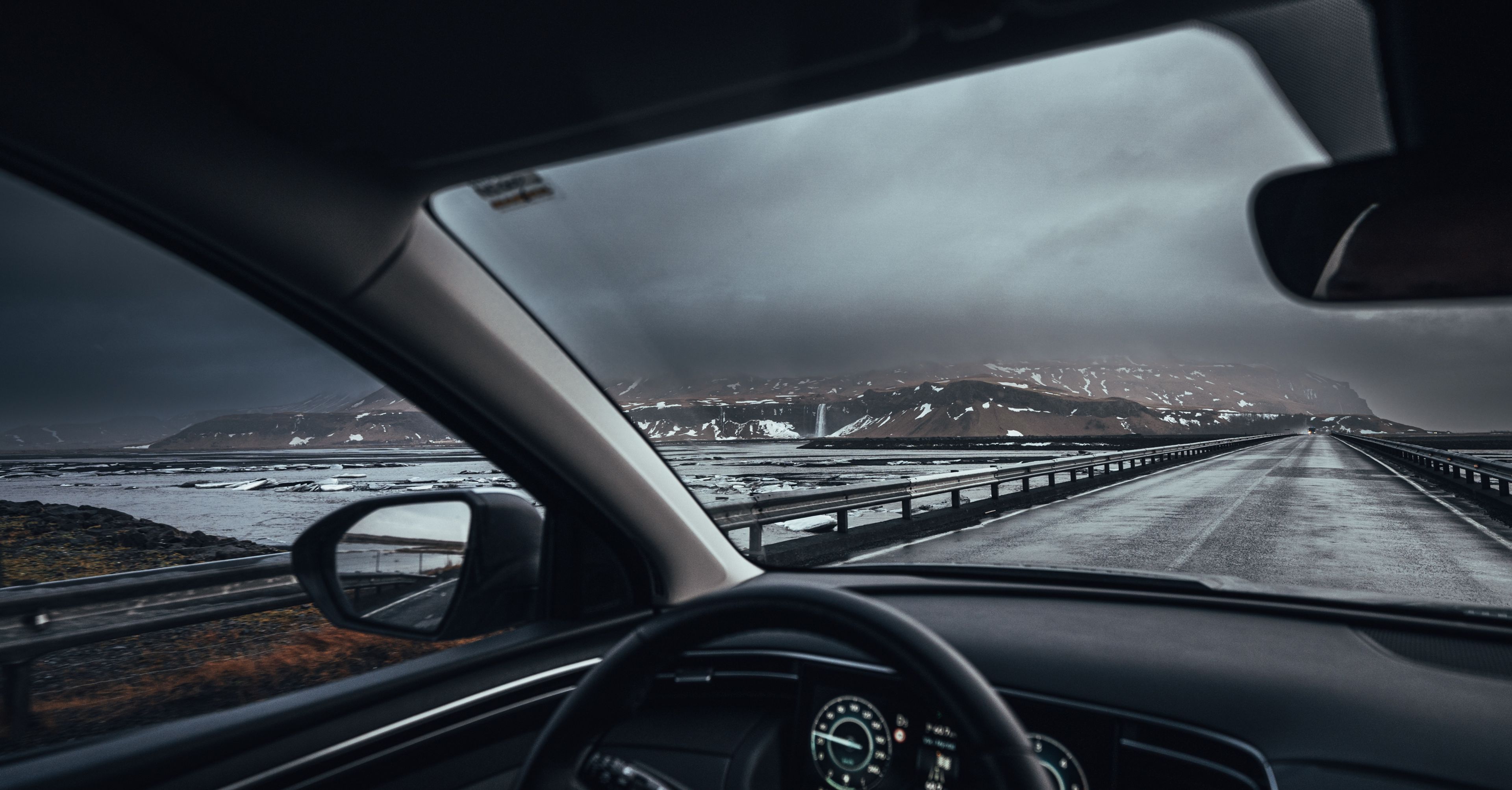 man driving in iceland, the hand on the wheel and the snowy icelandic landscape in the background 