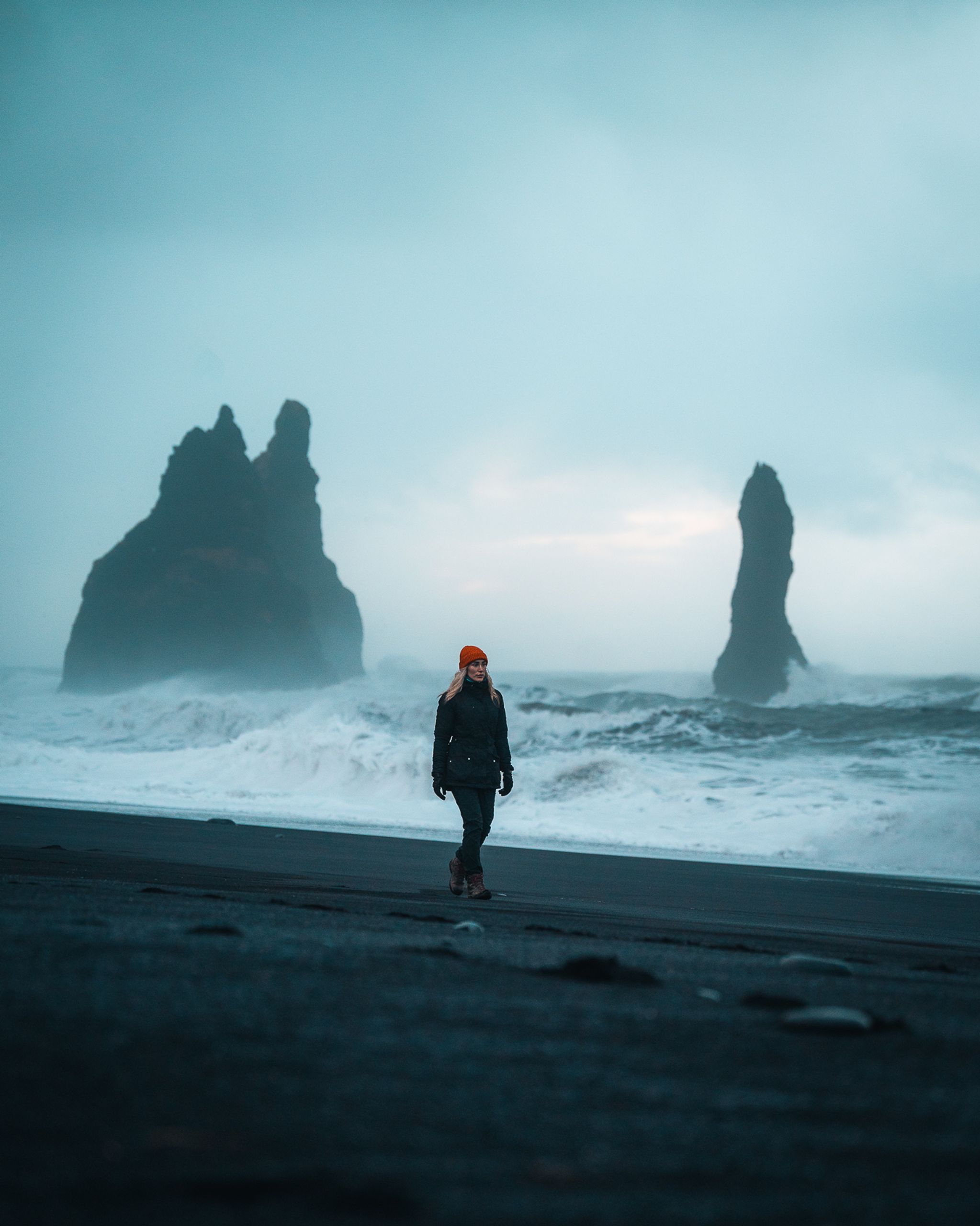 A woman walking on a black sand beach in iceland