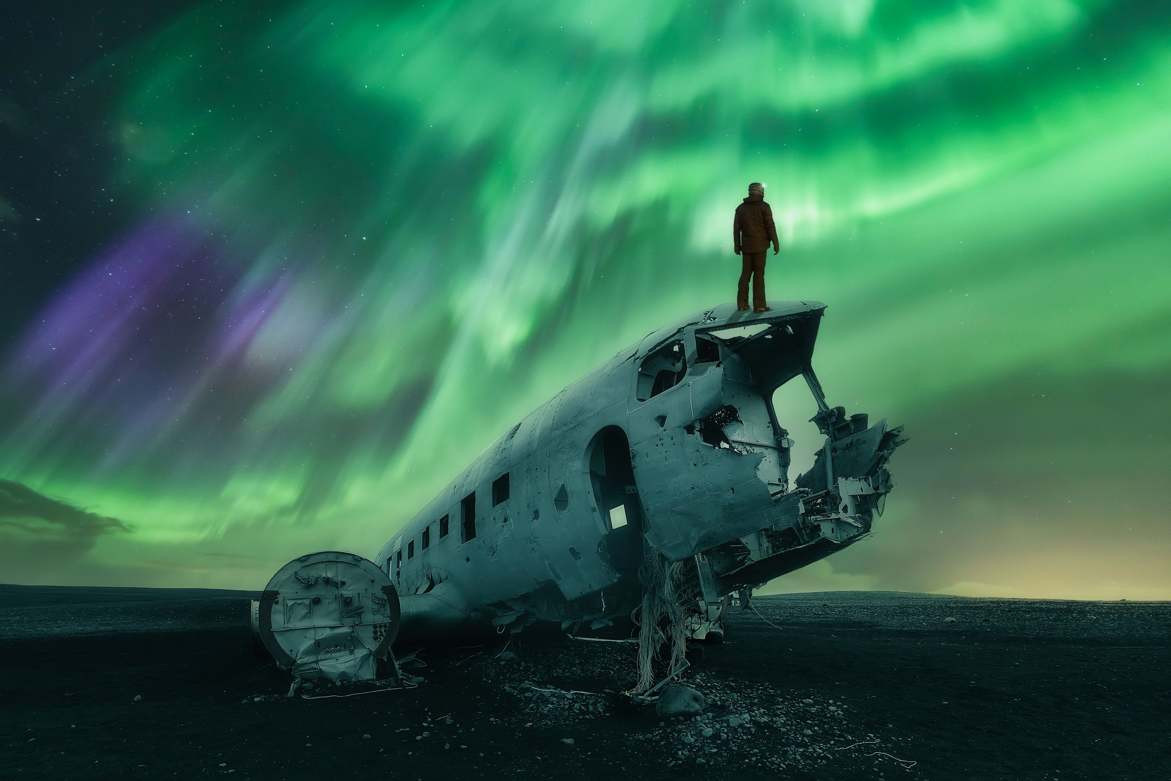 man standing on a plane during a northern lights show on one of iceland's black sand beaches