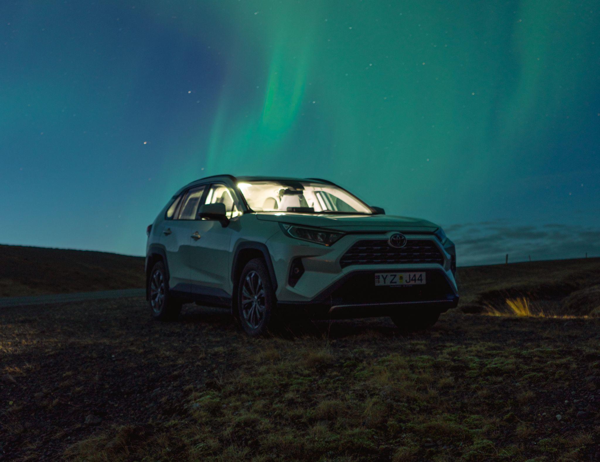 A Toyota Rav4 rental car under the mesmerizing display of the Northern Lights in Iceland