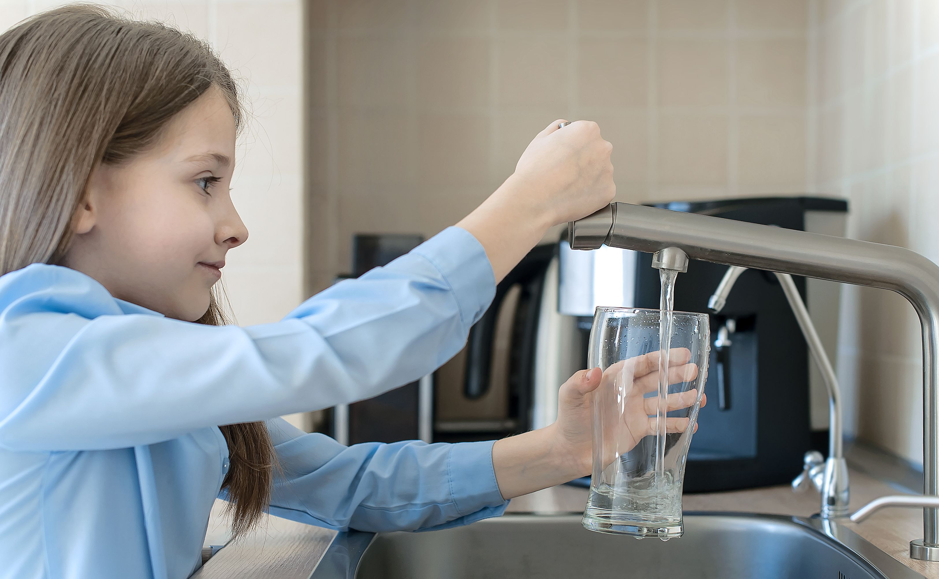 little girl with a blue shirt, serving herself a glass of tap water in Iceland 