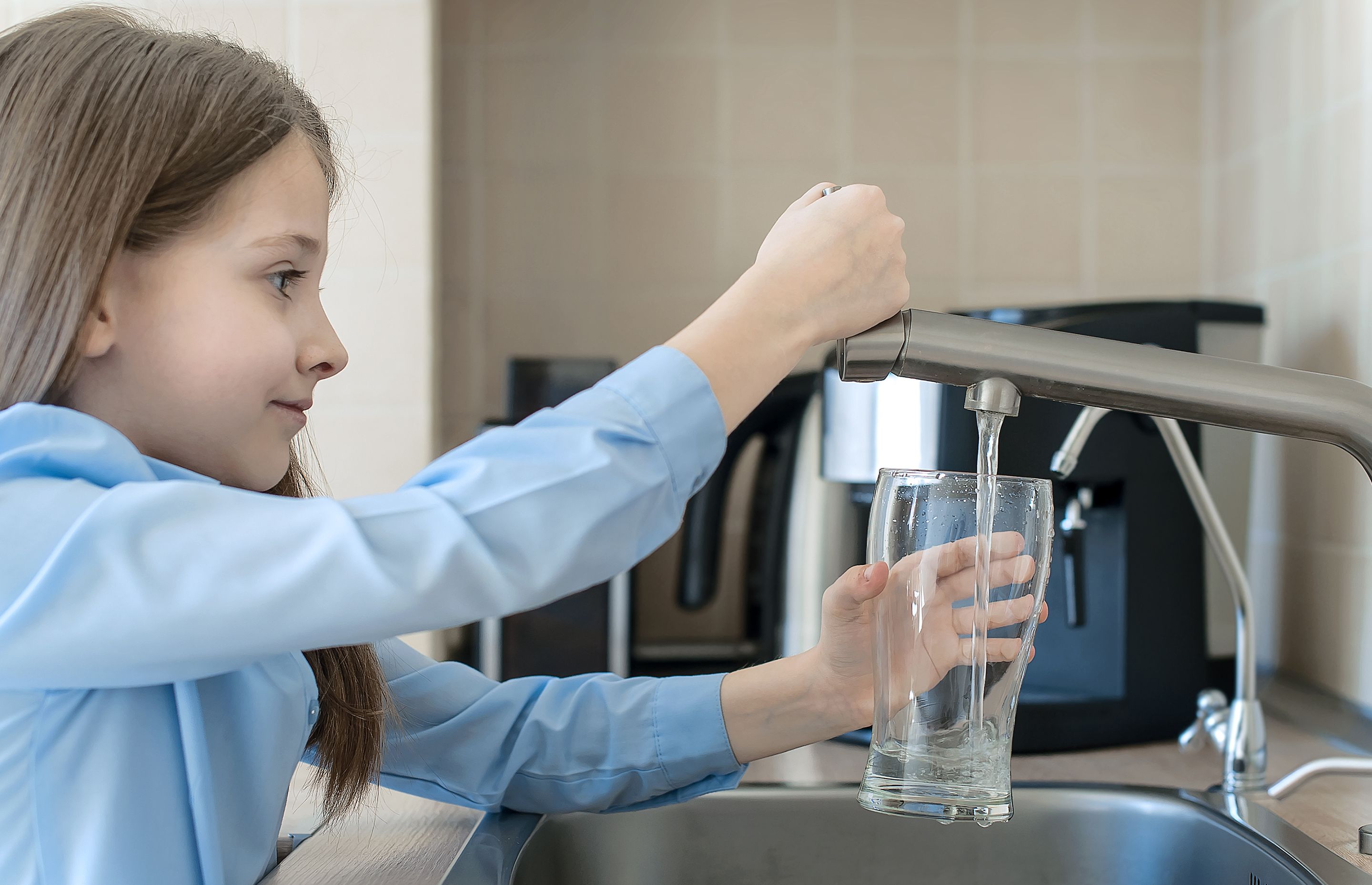 little girl with a blue shirt, serving herself a glass of tap water in Iceland 