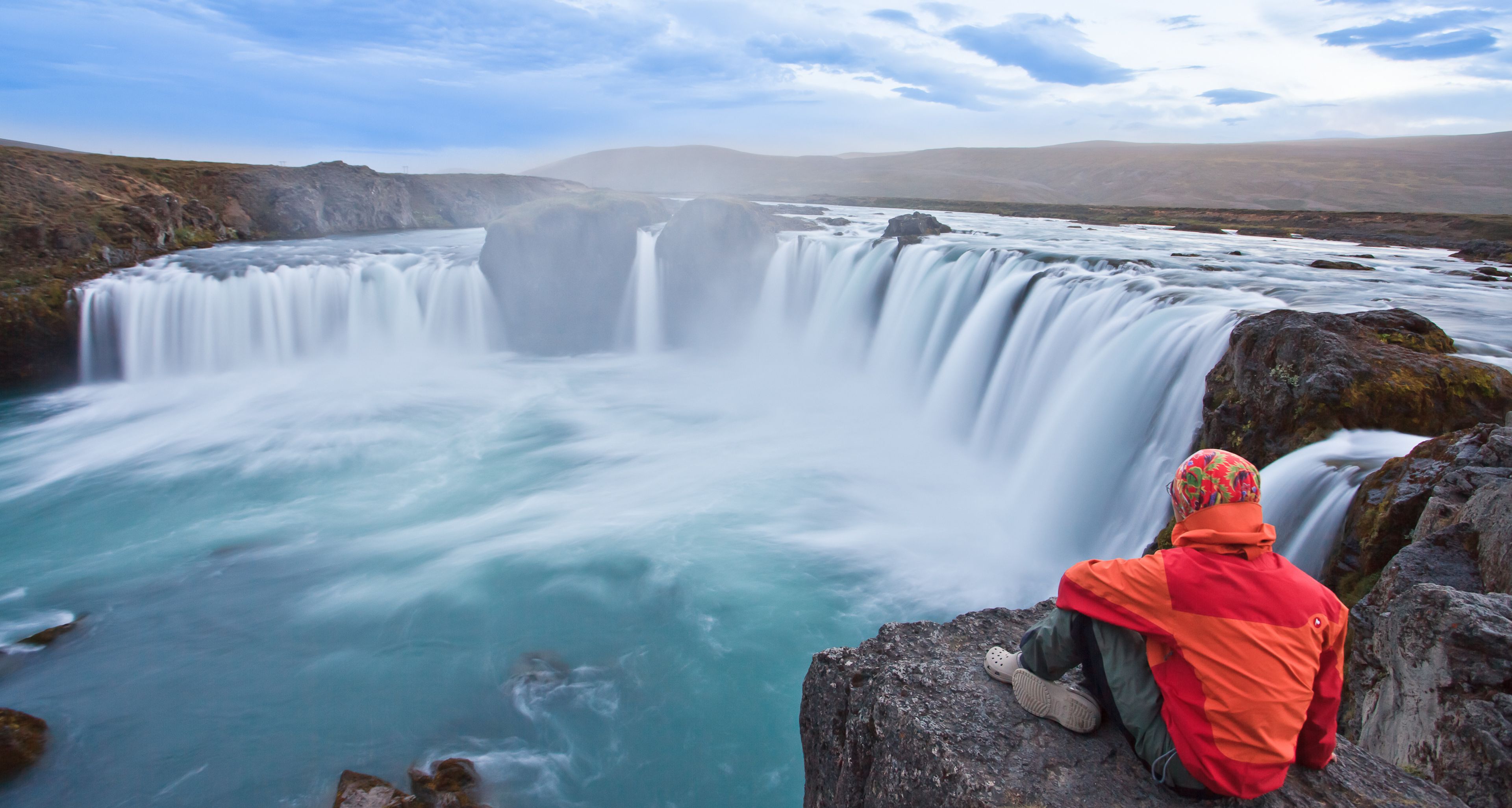 Hiker with a red jacket overlooking the beautiful waterfall Godafoss