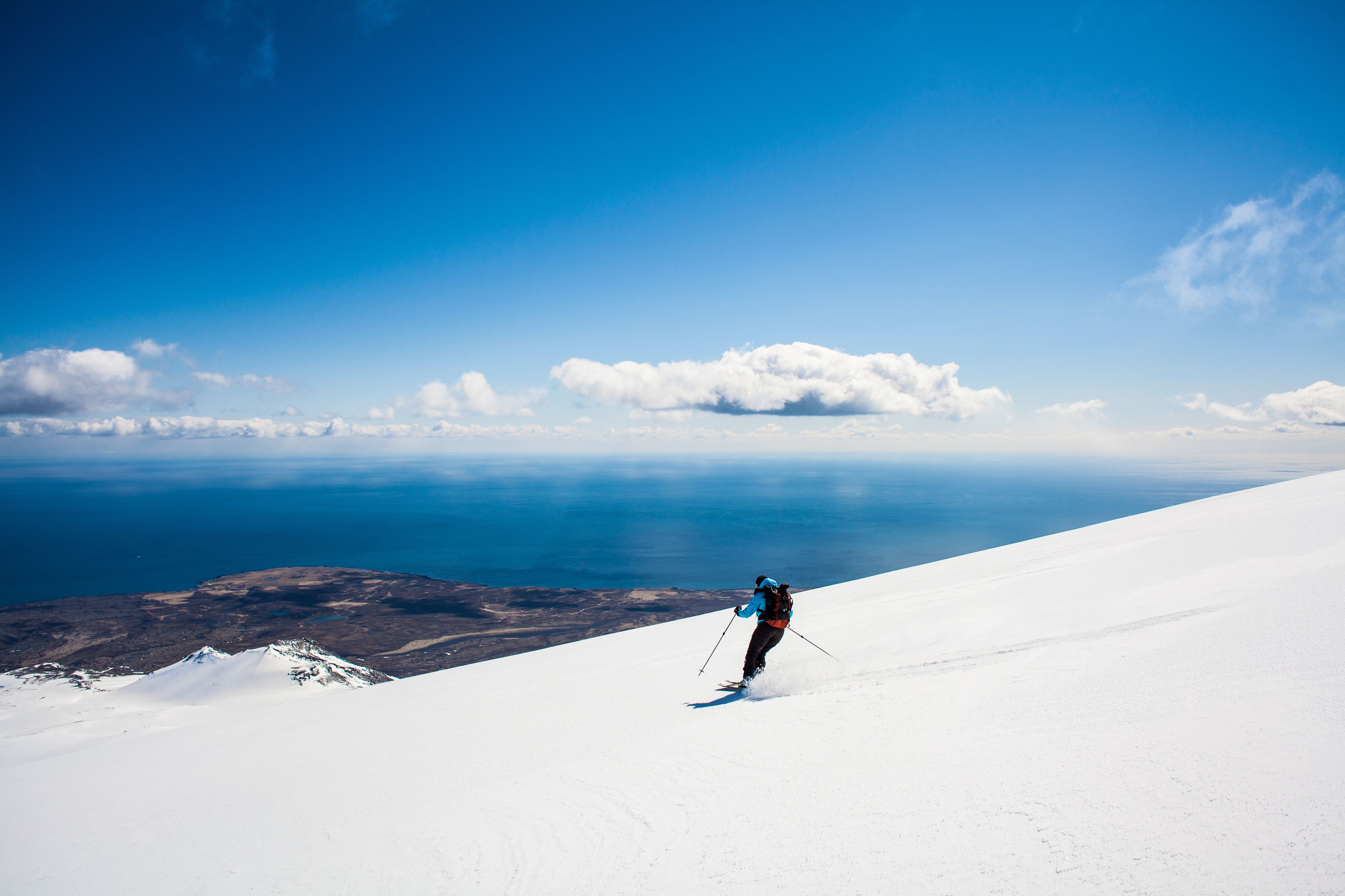 A female skier skiing down a volcano and the Atlantic ocean in the background, Iceland