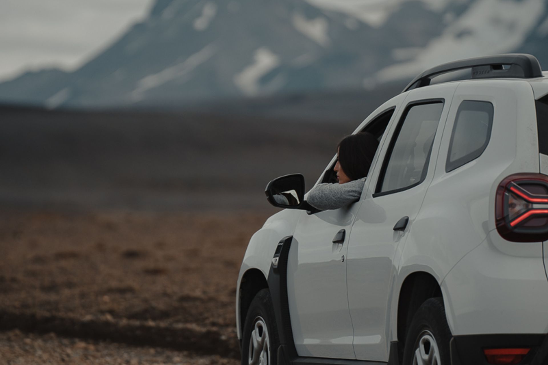 Woman observing the mountainous landscapes of Iceland from her car, a white Dacia Duster