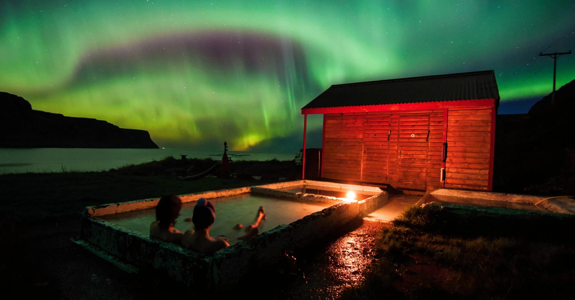 Relaxing in geothermal hot pool under northern lights in Iceland in October