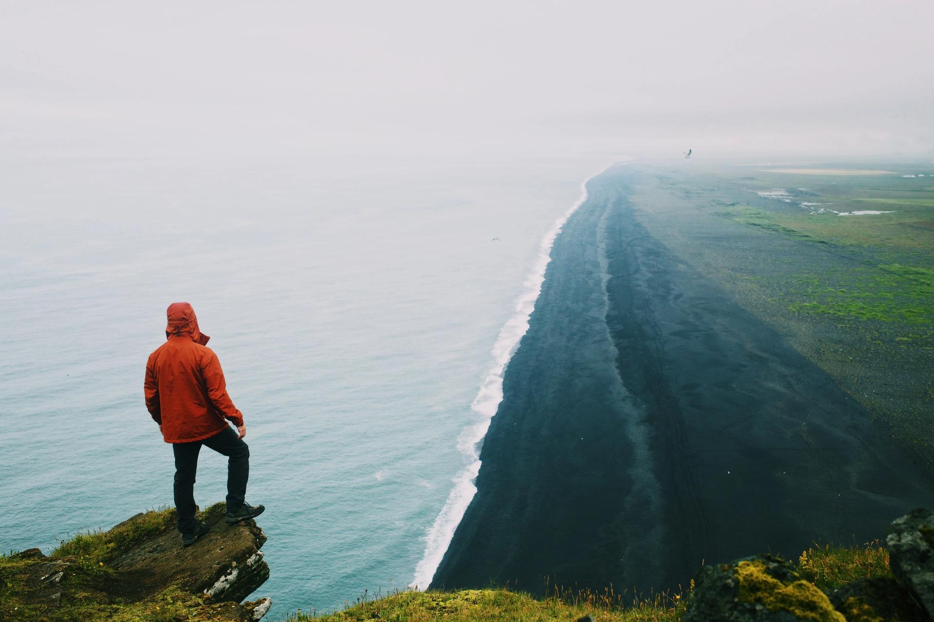 A man standing on a cliff edge above the ocean at a black sand beach by the Dyrhólaey in Icelaand