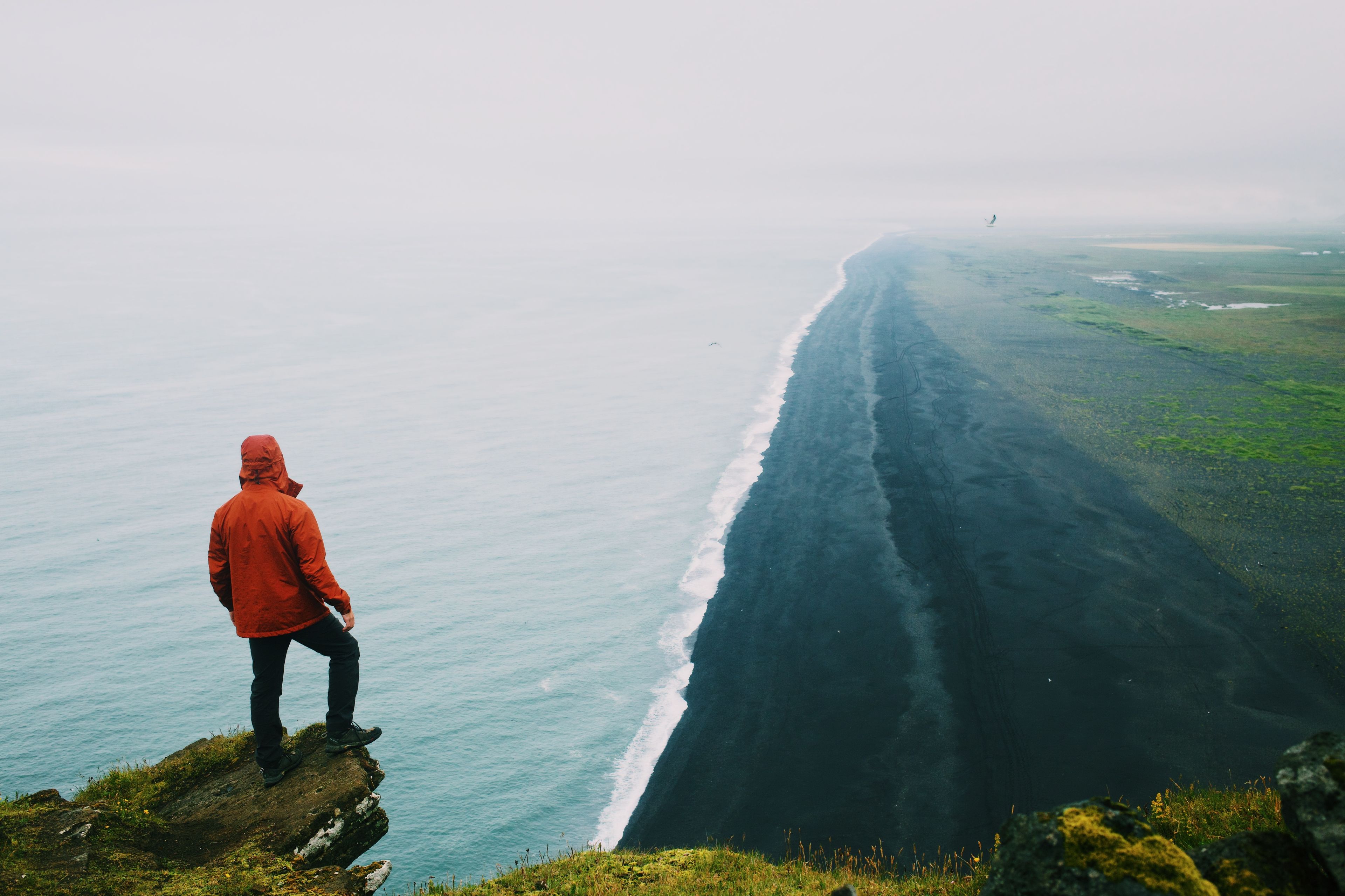 A man standing on a cliff edge above the ocean at a black sand beach by the Dyrhólaey in Icelaand