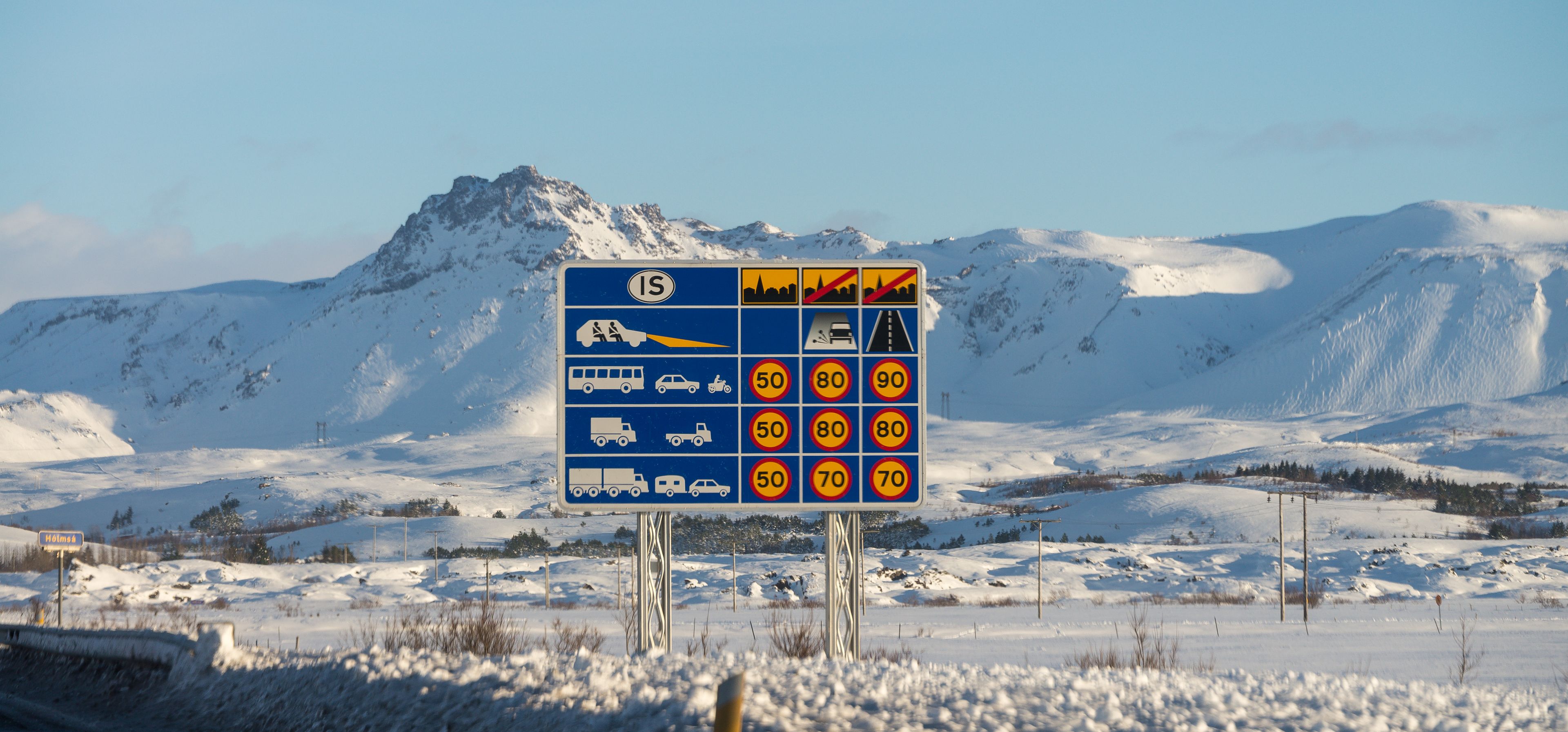 sign on Icelandic roads showing speed limits, picture taken in winter with view on snowy mountains in background 
