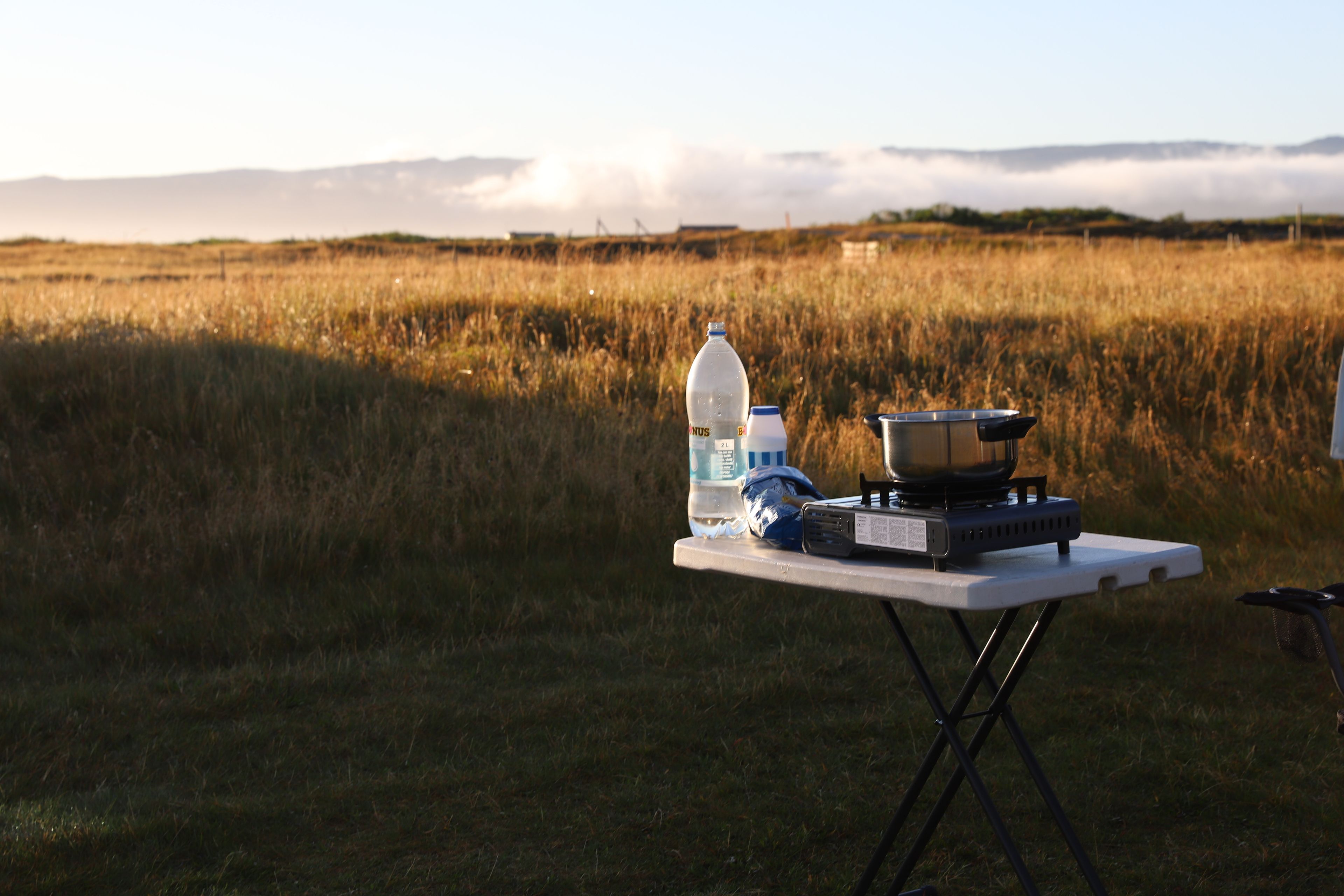 Mesa, botella de agua, bolsa de pasta, camping gas y olla en un paisaje de Islandia