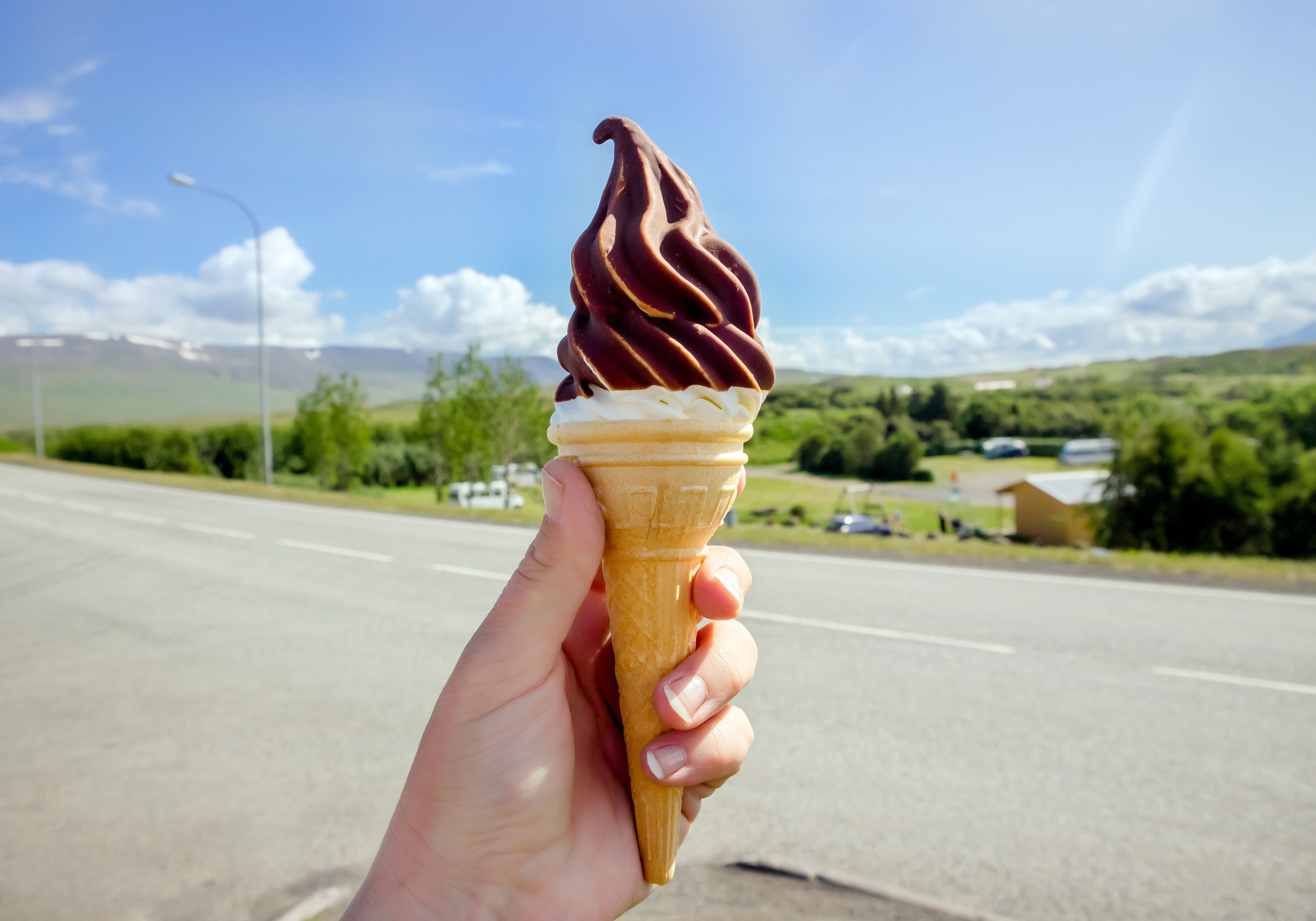 Hand holding Icelandic local vanilla ice cream dipped in hot chocolate