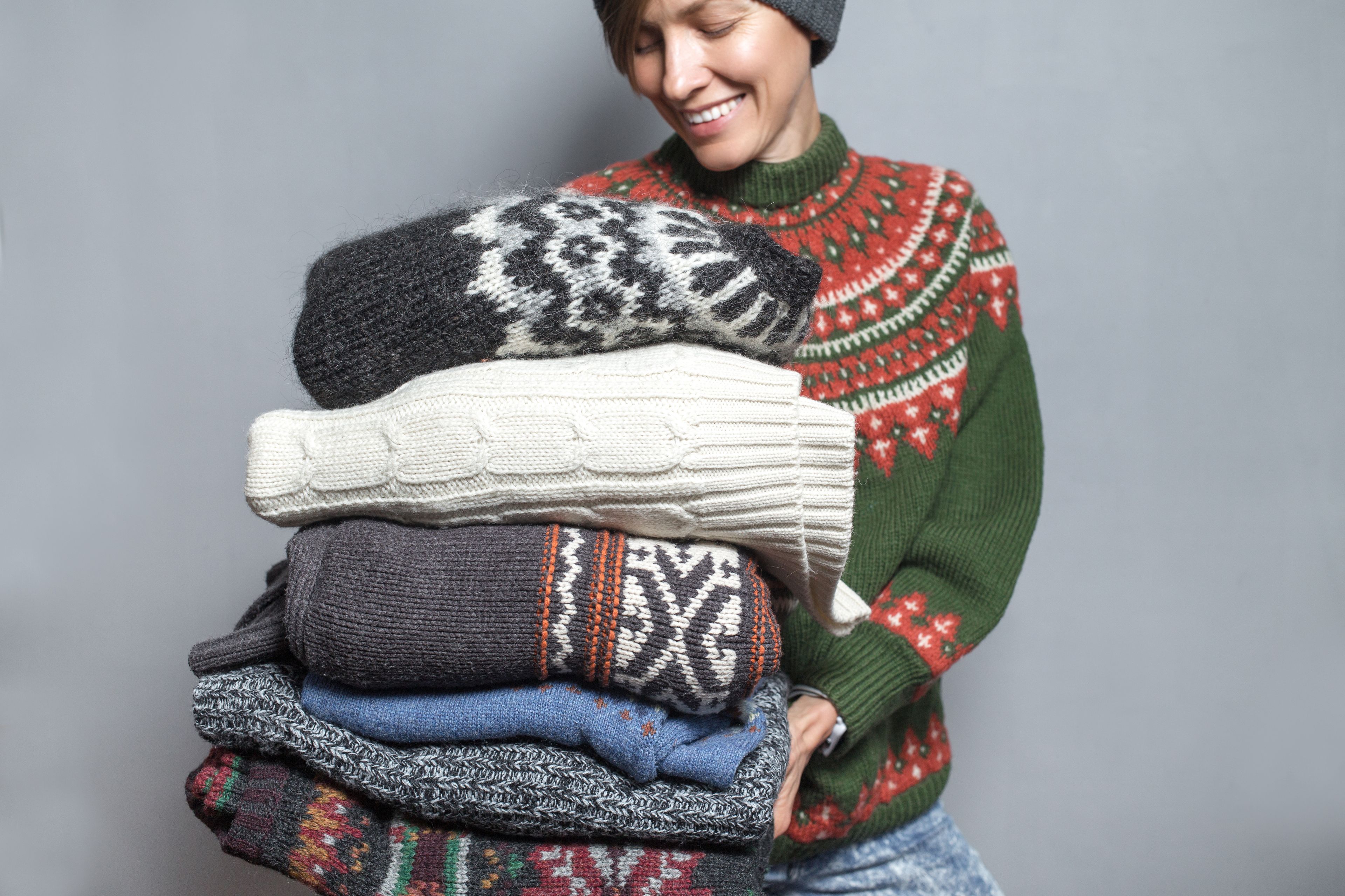 Young woman holding a pile of sweaters wearing knitted hat and wool sweater