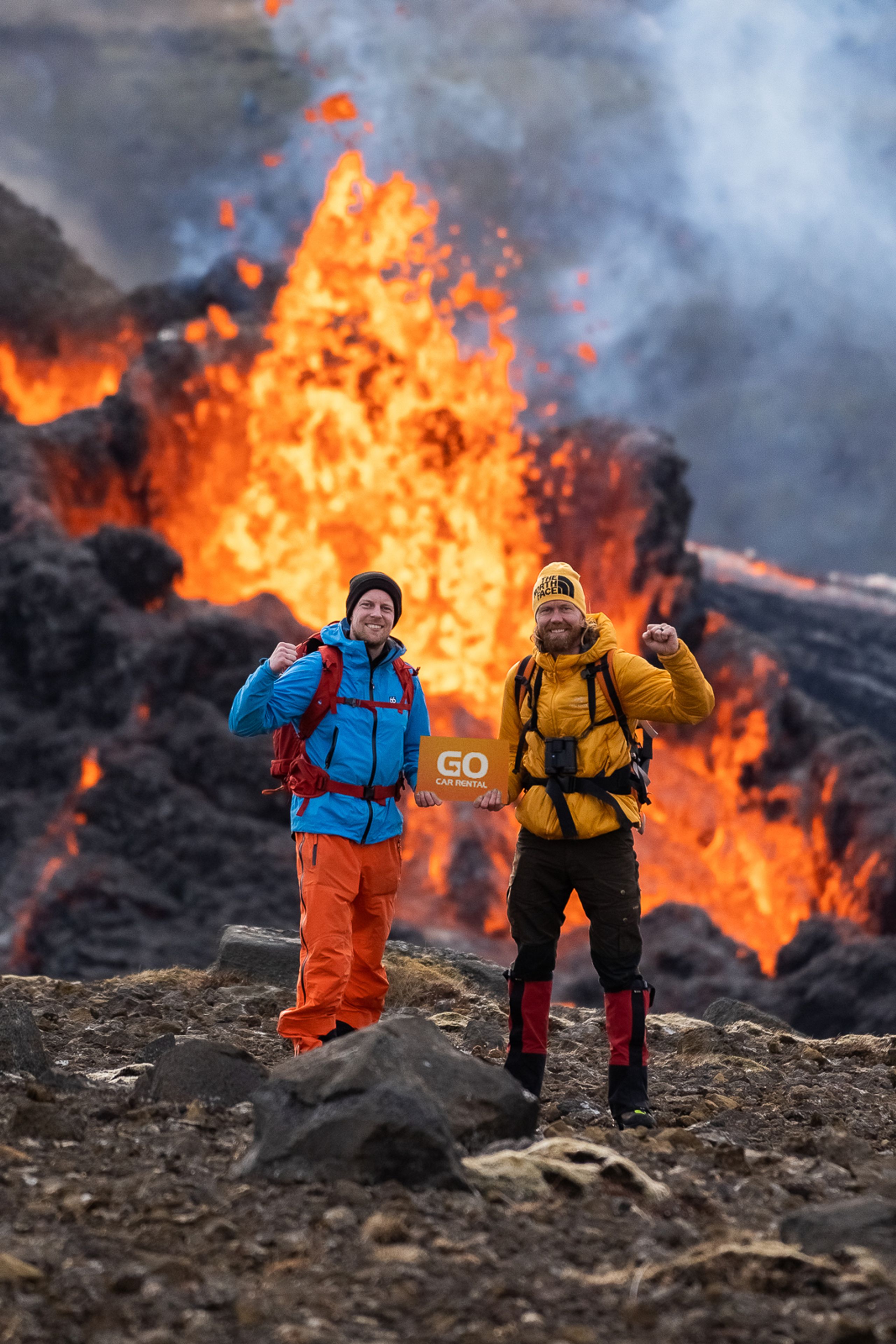 Owners of Go Car Rental company Iceland standing next to a volcano holding their rental car brand name, best car rental in Iceland