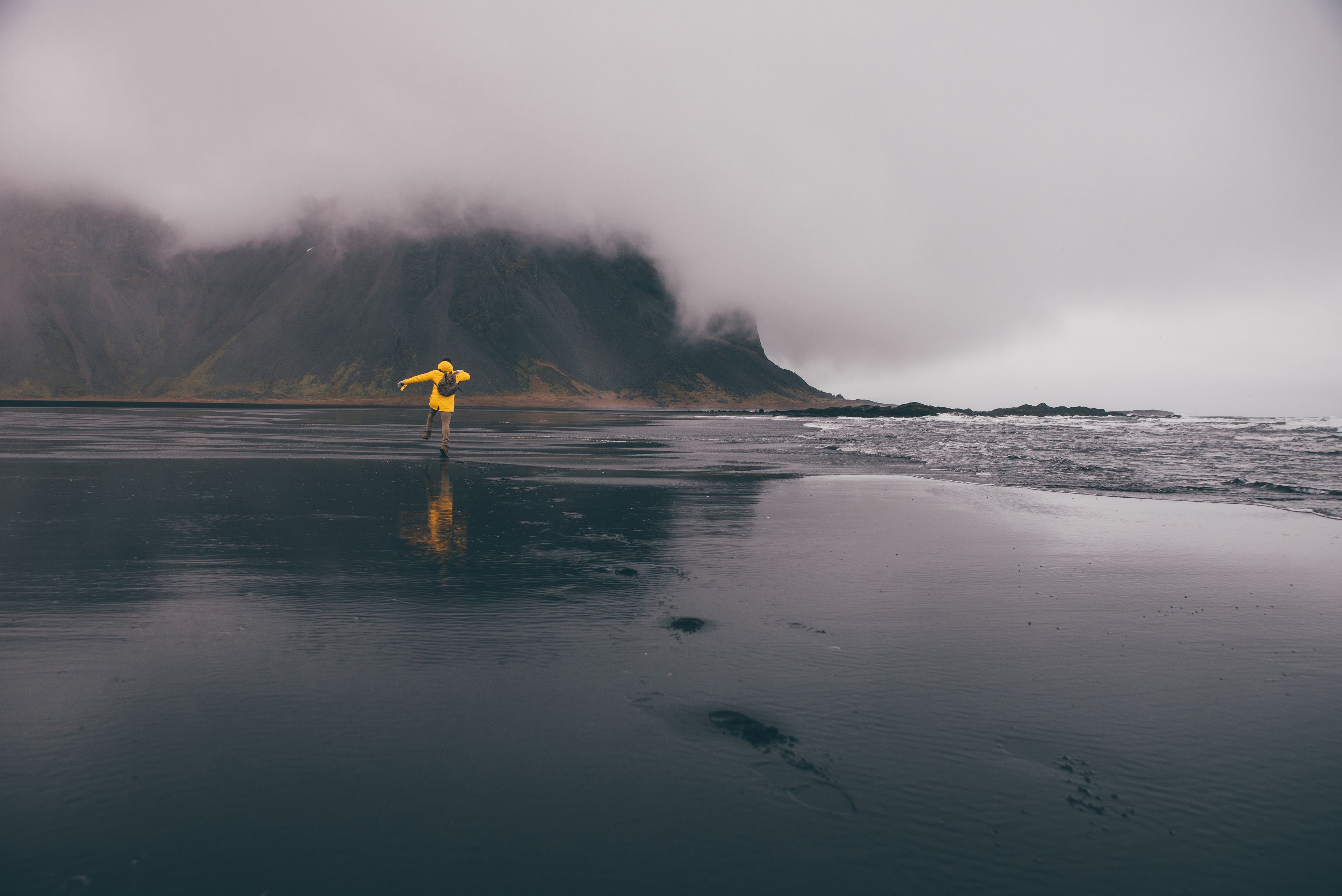 Persona con una chaqueta amarilla corriendo por una playa de arena negra en Islandia