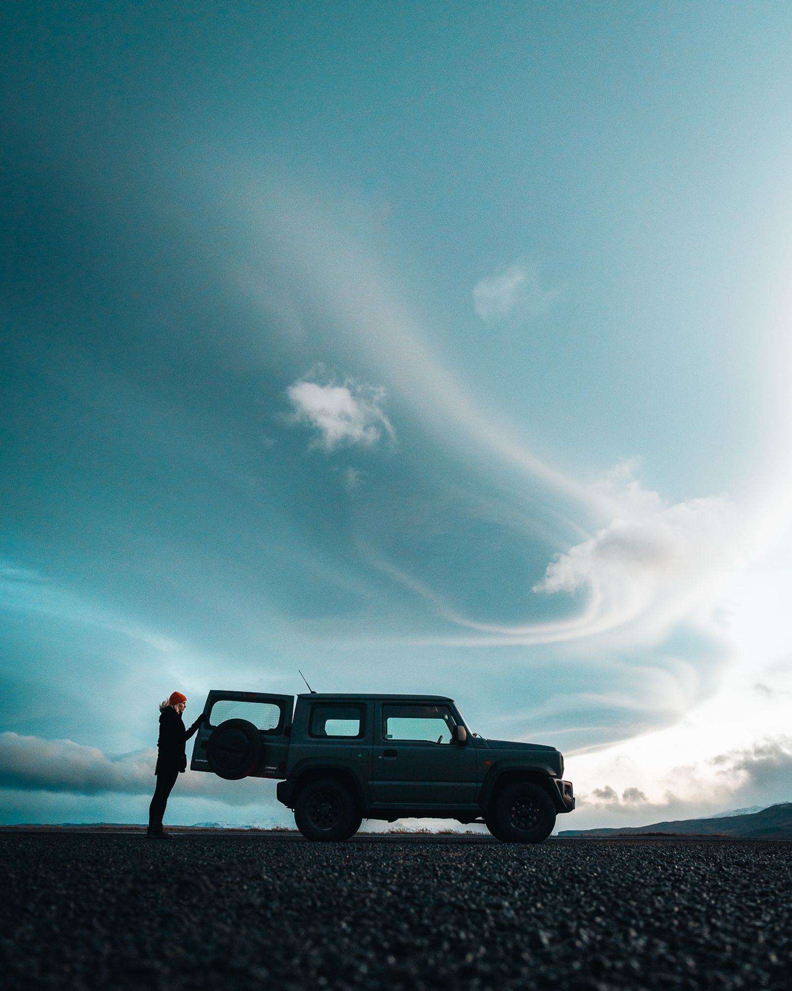 A woman standing next to her rental car watching the Iceland landscape