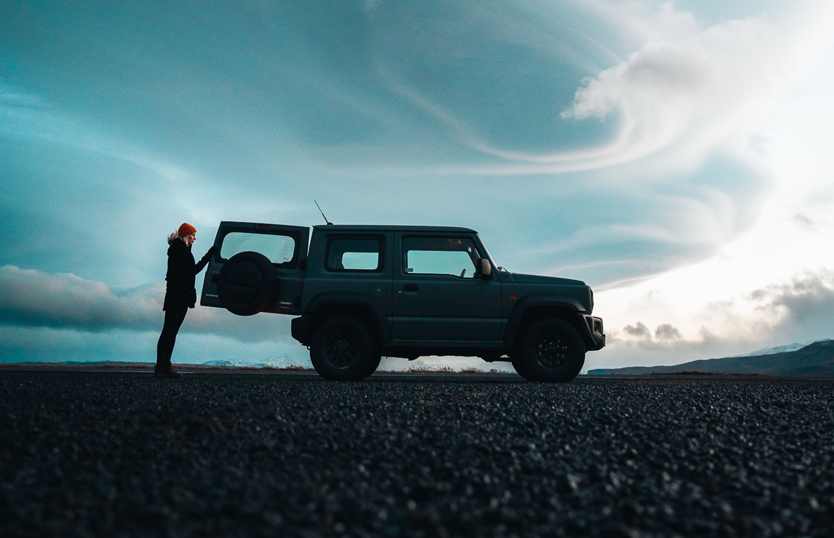 A woman standing next to her rental car watching the Iceland landscape