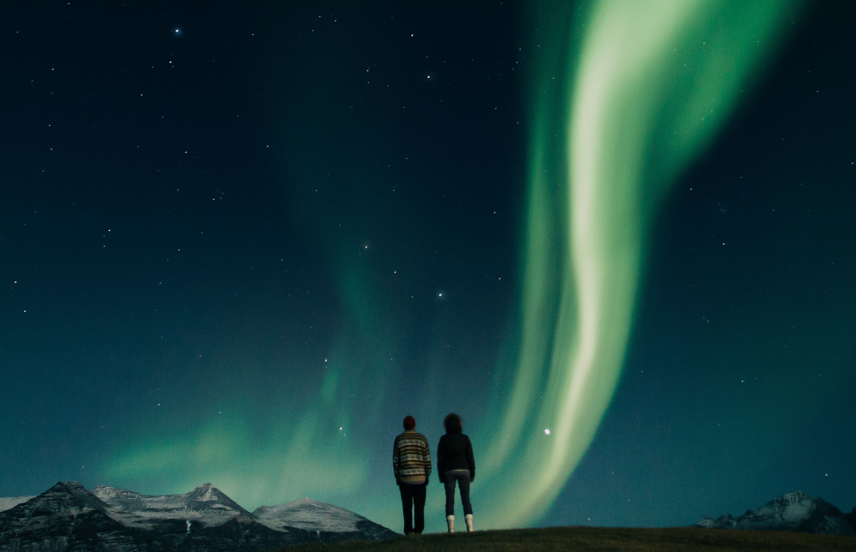 Couple admiring aurora borealis in the blue and starry sky of iceland in winter time 