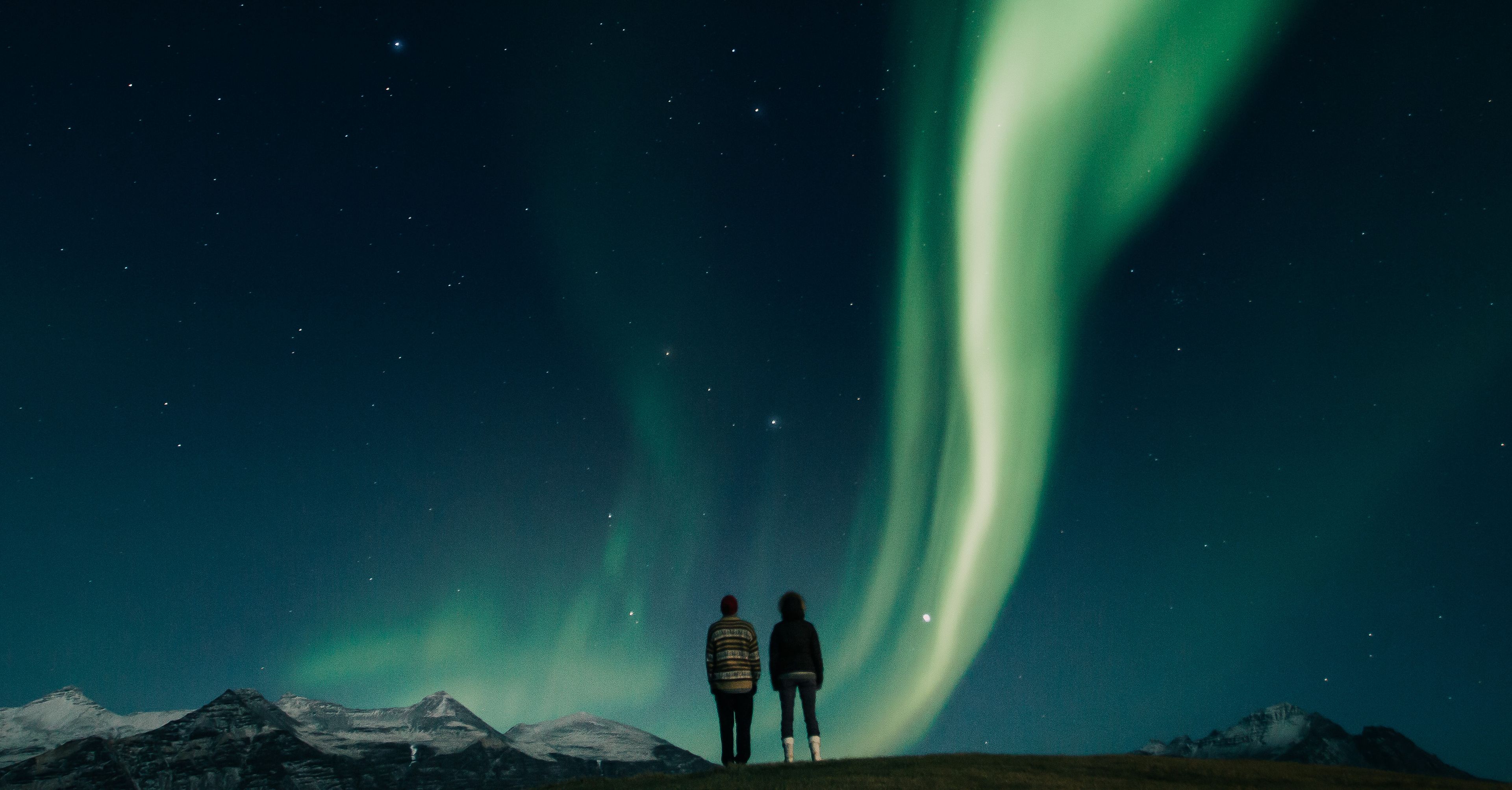 Couple admiring aurora borealis in the blue and starry sky of iceland in winter time 