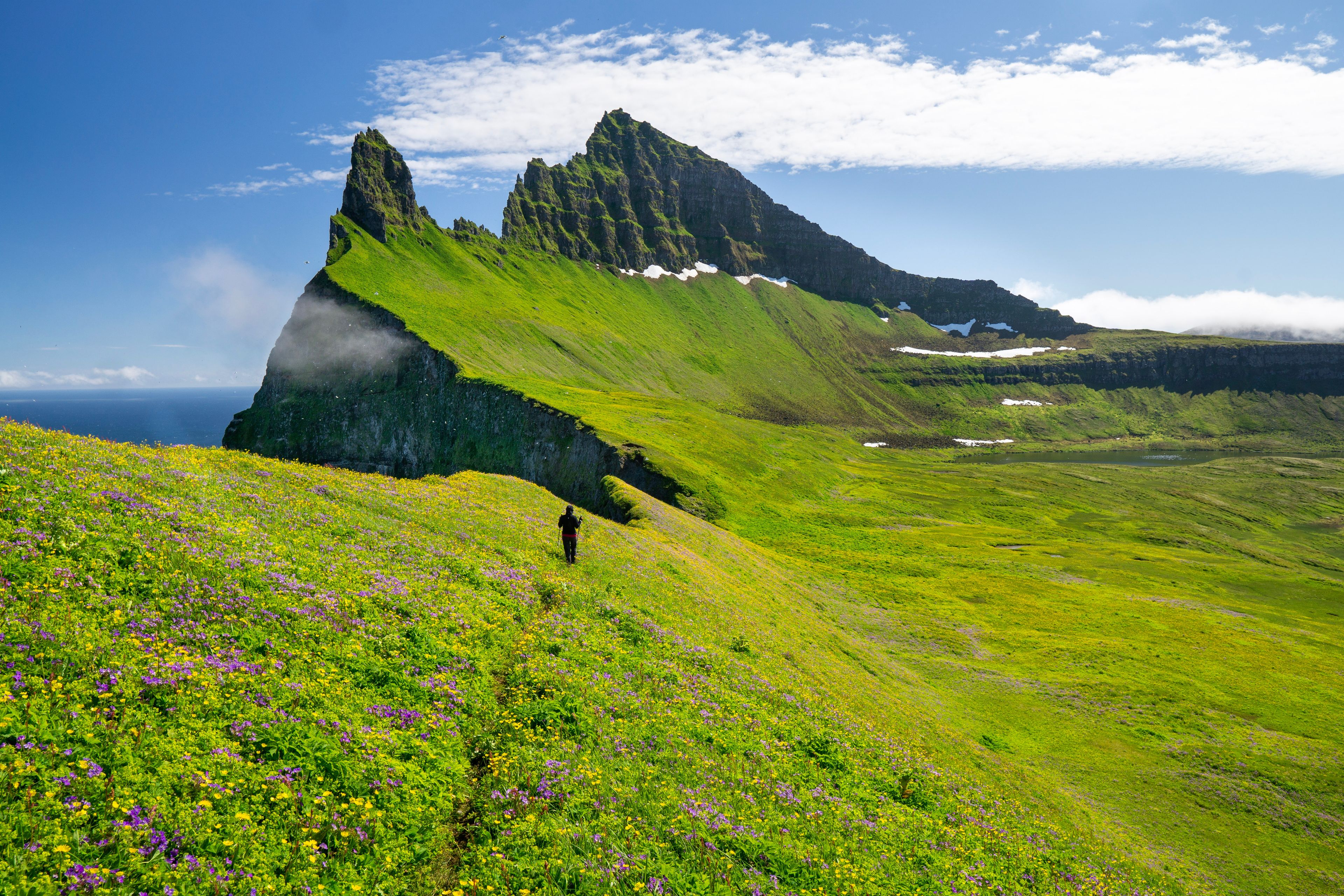 A persons wearing warm clothes in a lush landscape with bright sunlight while visiting iceland in july