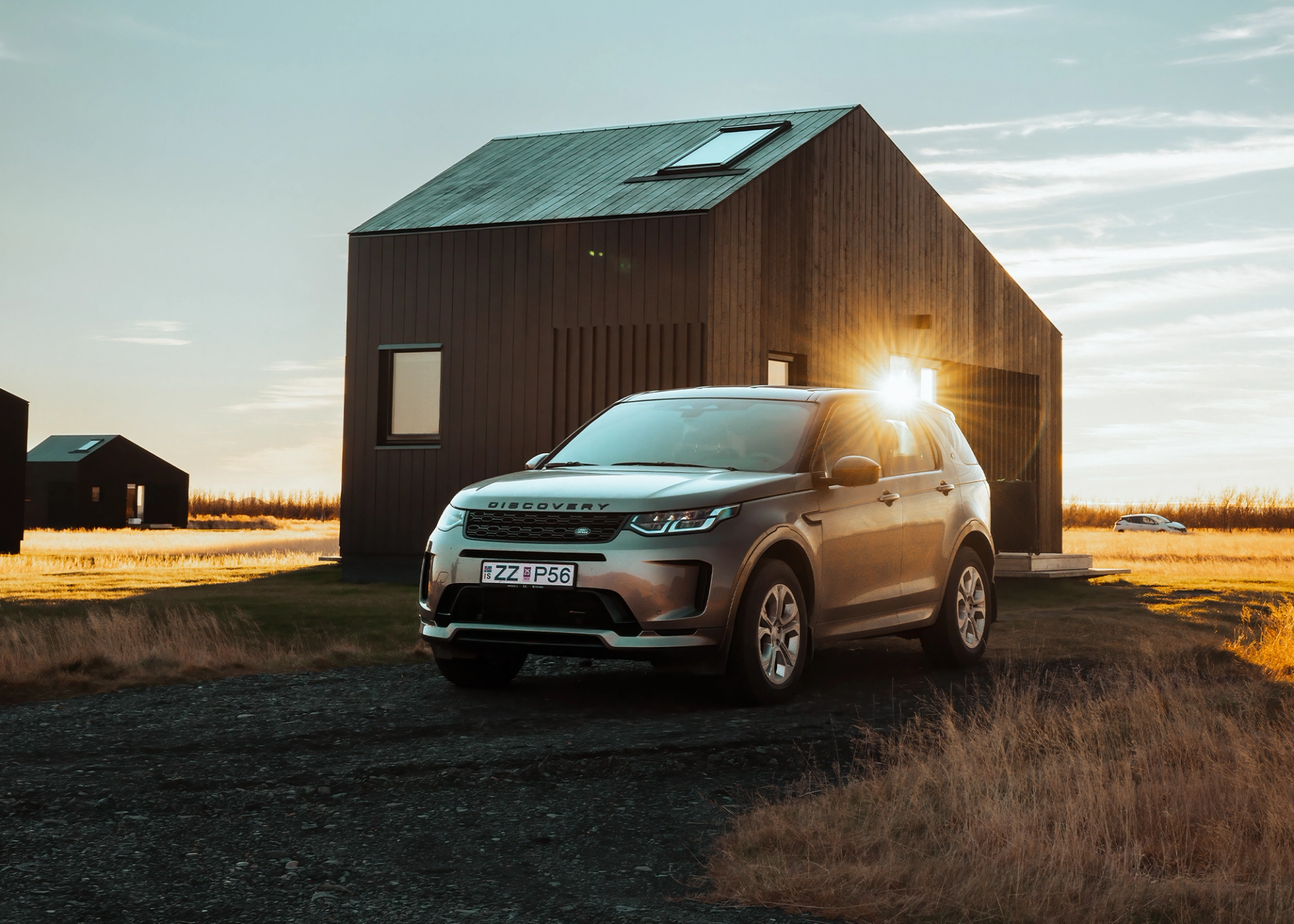 Dark gray Land Rover Discovery Sport rental car parked near a brown house