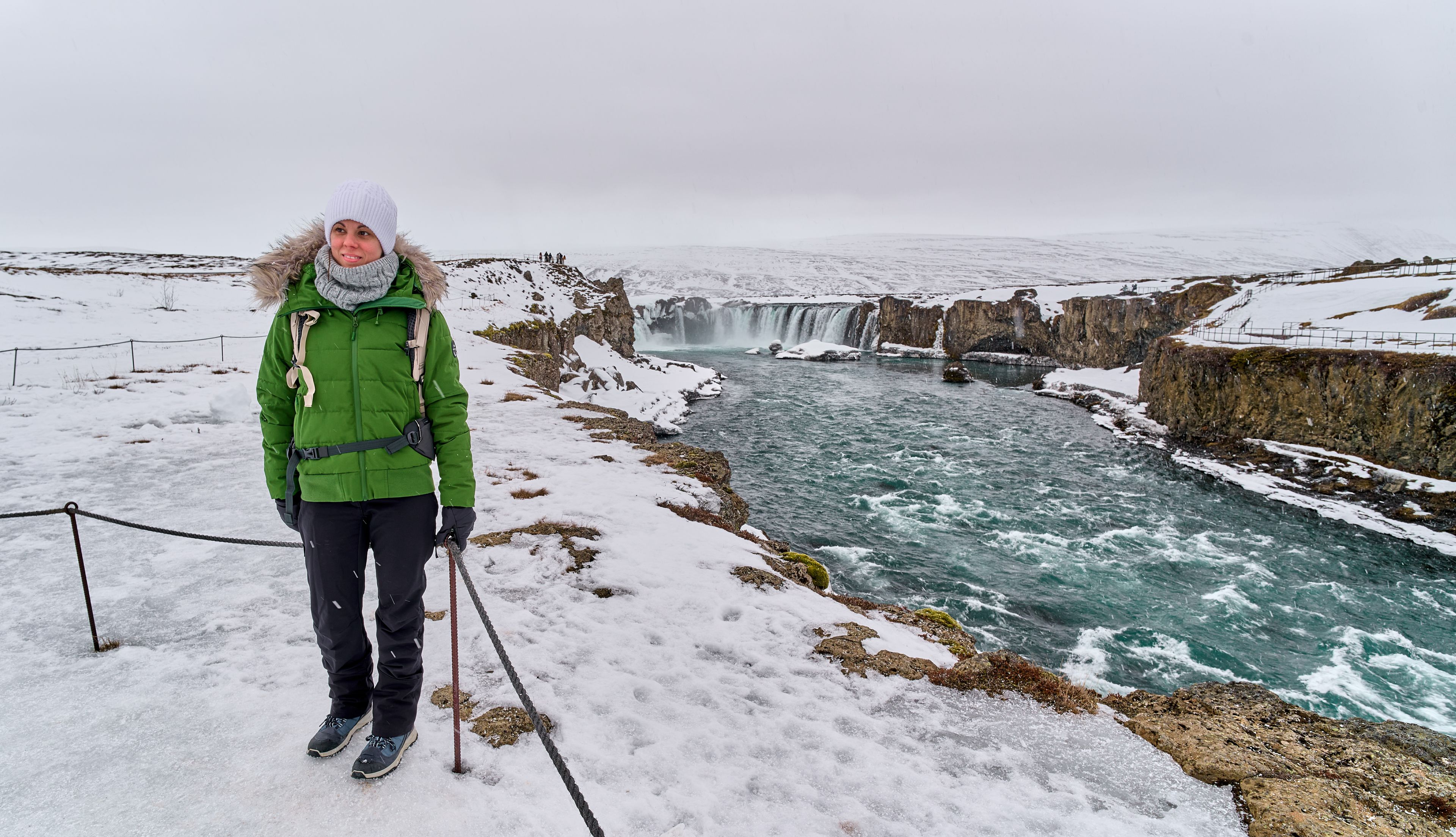 Chica vestida con capas, bufanda, y gorro en frente de una cascada en Islandia