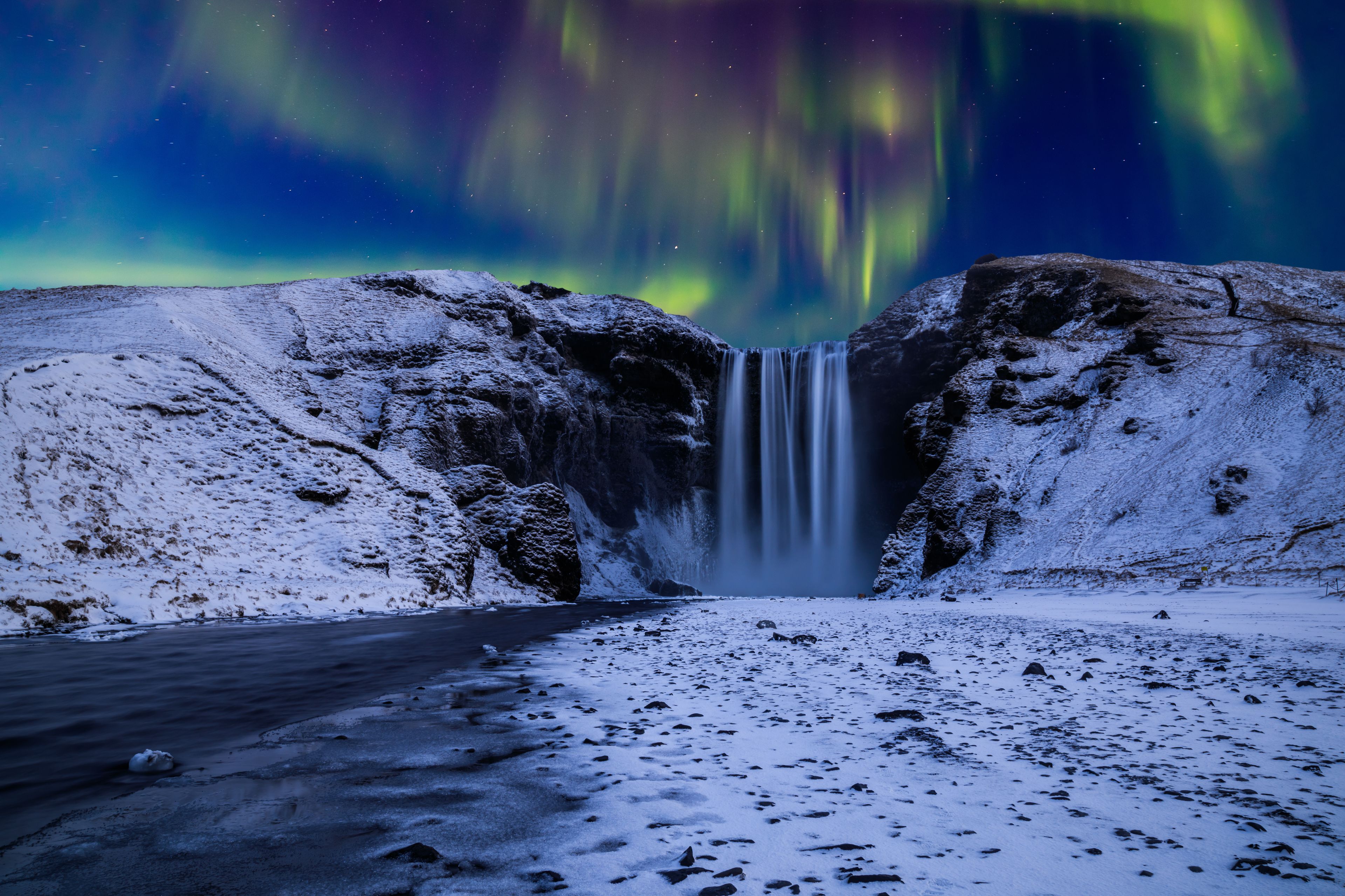 Skógafoss covered in snow under the Northern Lights