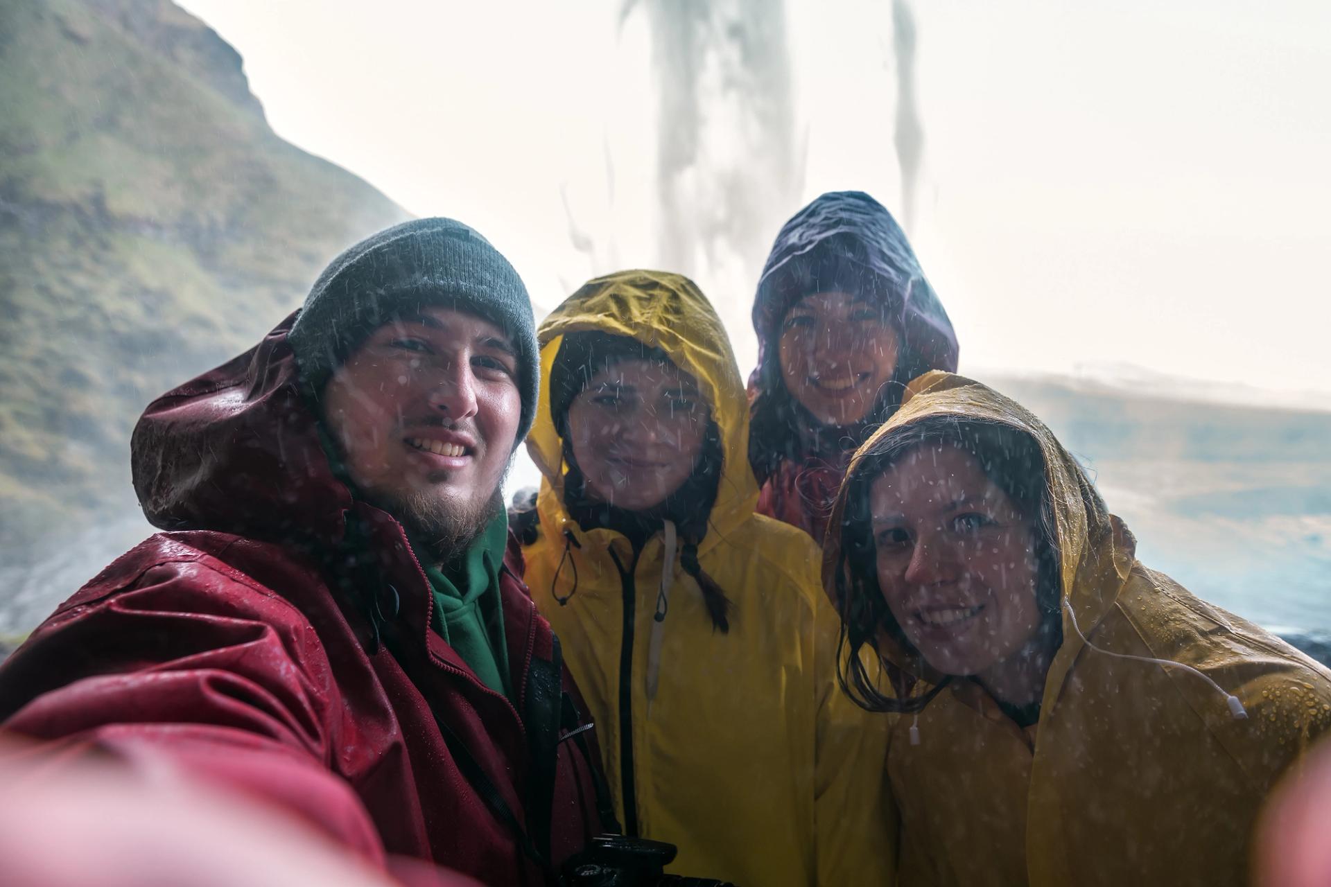 four friends wearing rain jackets inside seljalandsfoss waterfall in Iceland