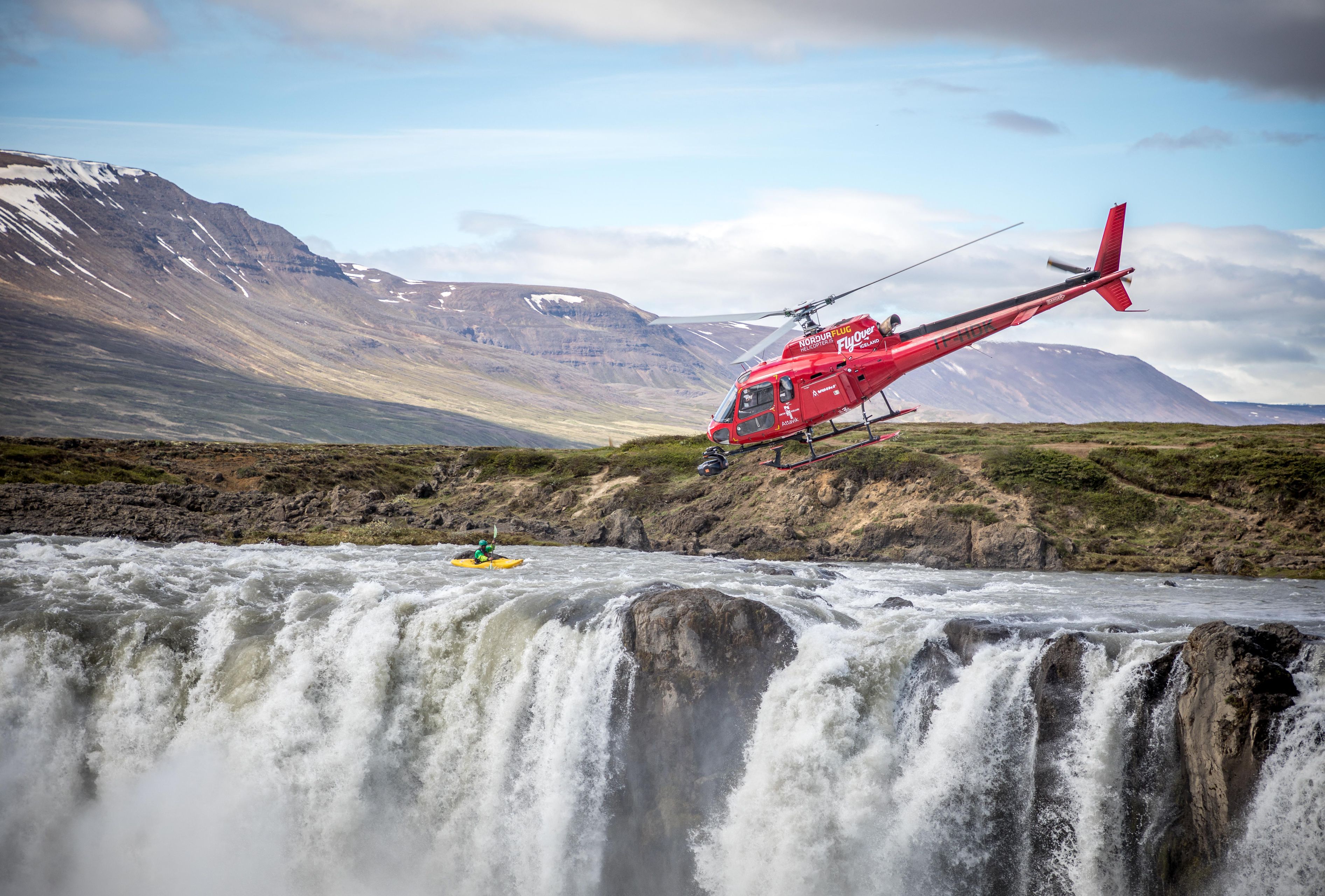 a helicopter flying over a waterfall to film iceland for flyover iceland
