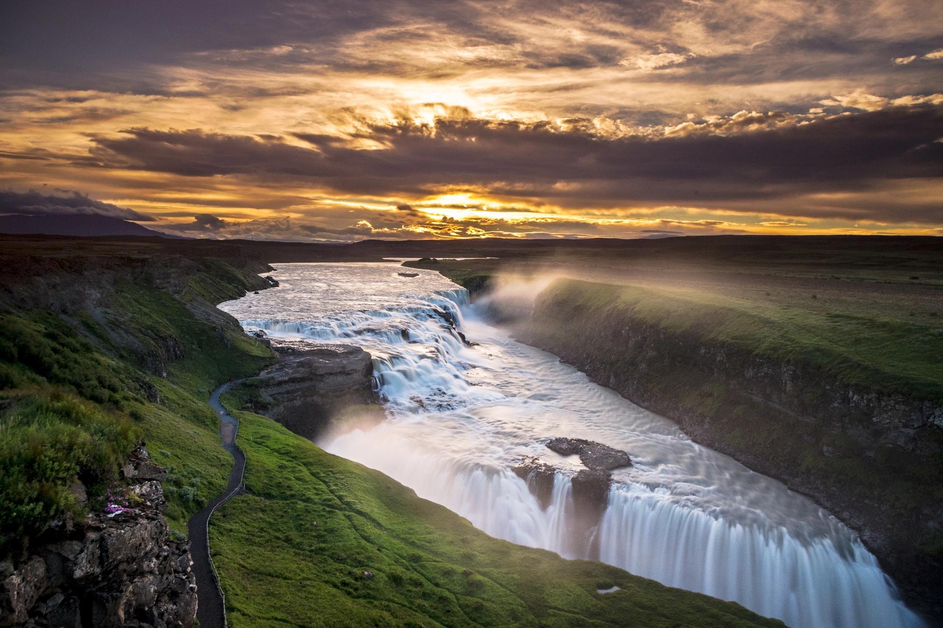 Gullfoss waterfall plunging into a deep canyon with misty rainbow and dramatic landscape