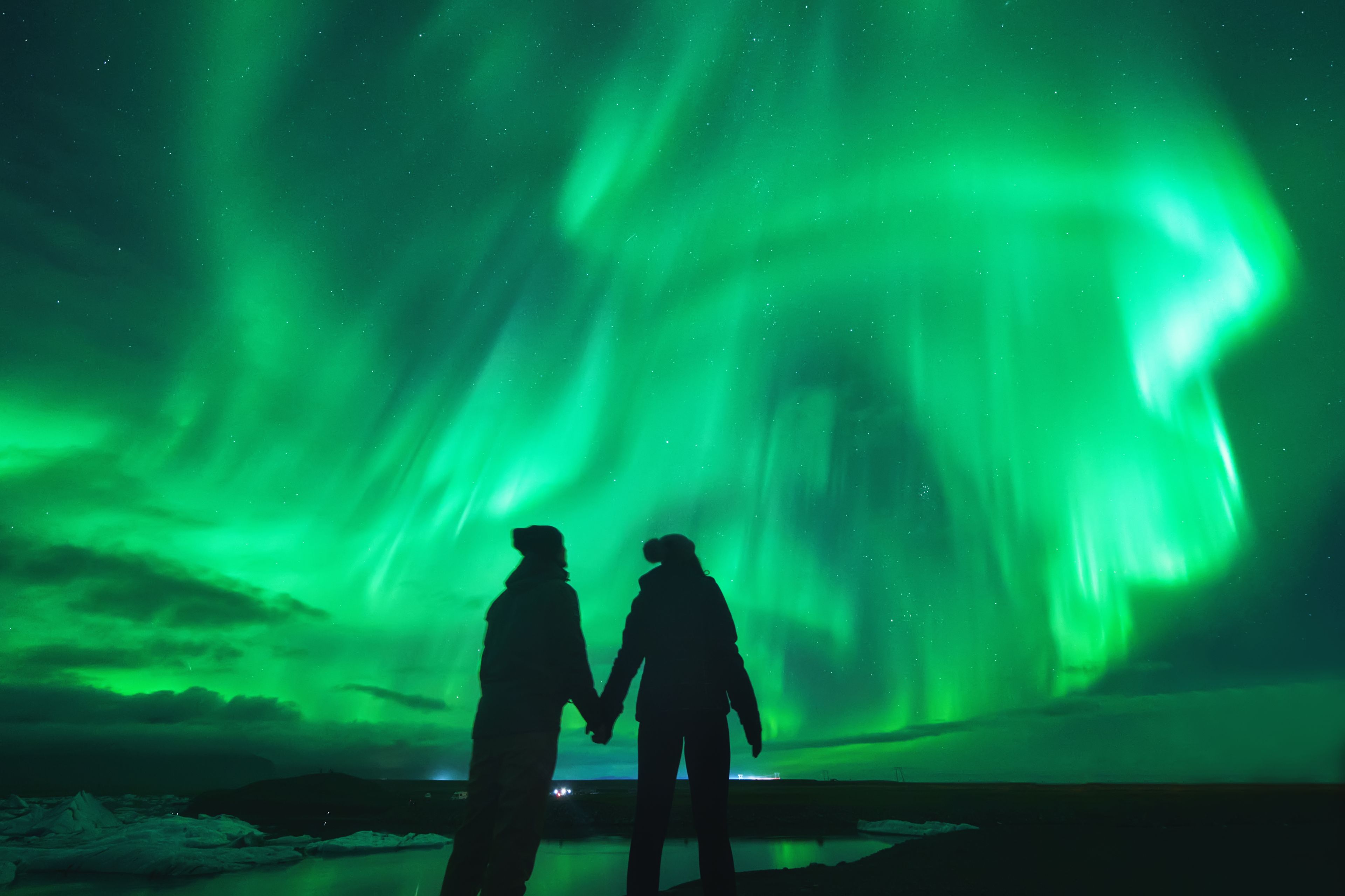 A view of couple watching aurora dancing in the sky during a cold weather on a road trip at a black sand beach