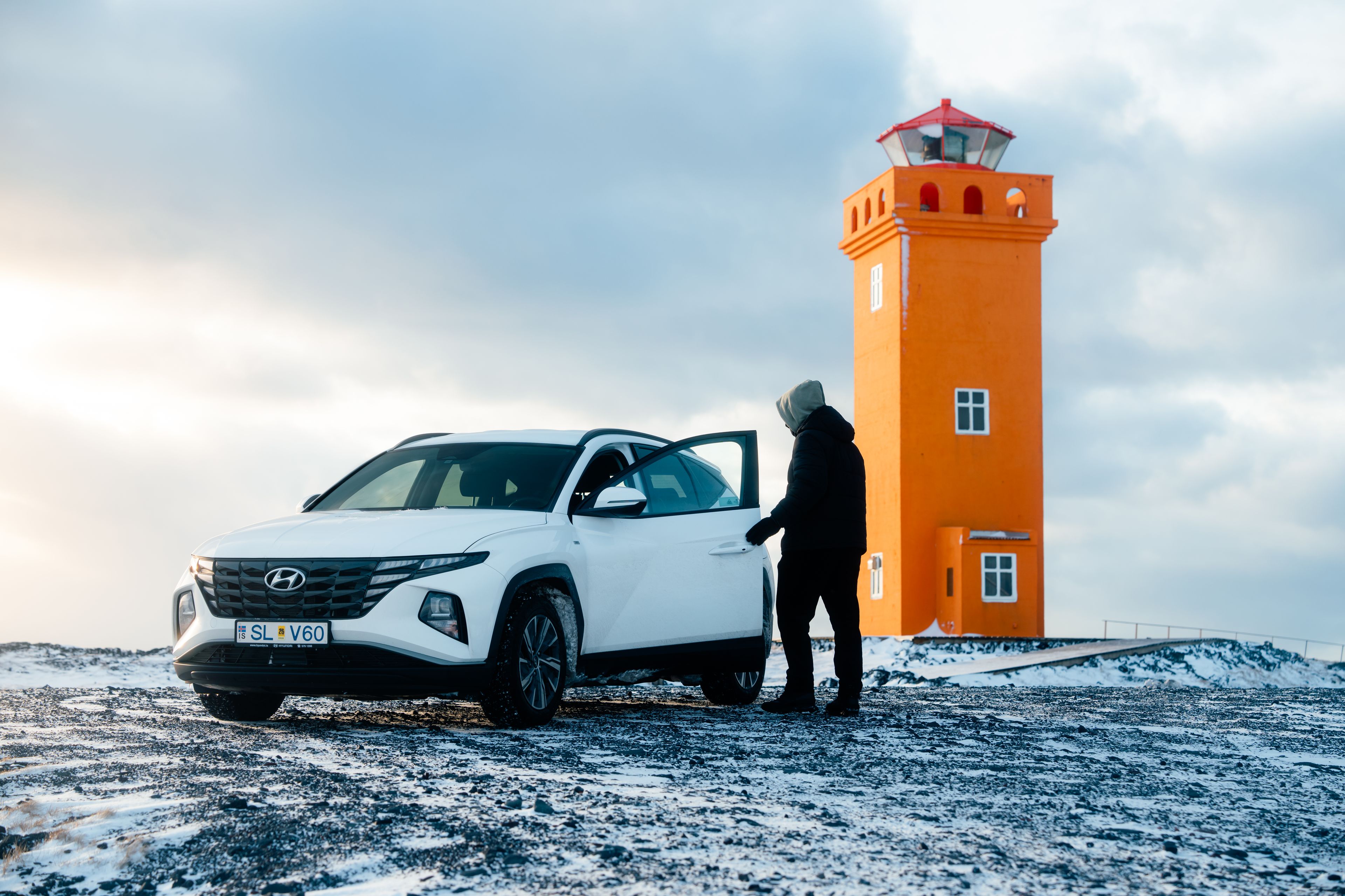 a man walking into his Hyundai Tucson 4x4 rental car during a snowy winter with a orange lighthouse in the background