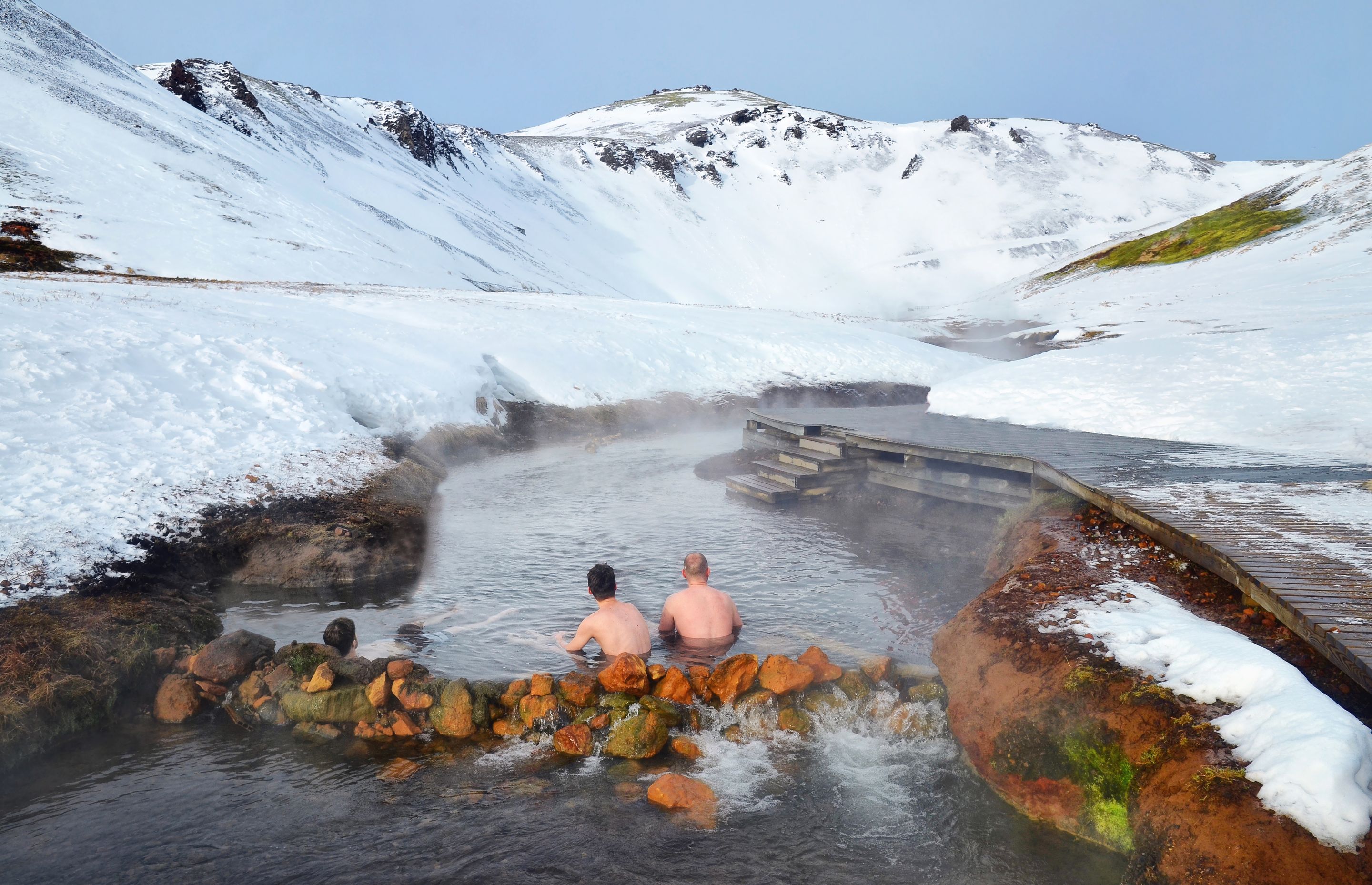 People sitting in Hot river in Iceland in winter snowy mountains