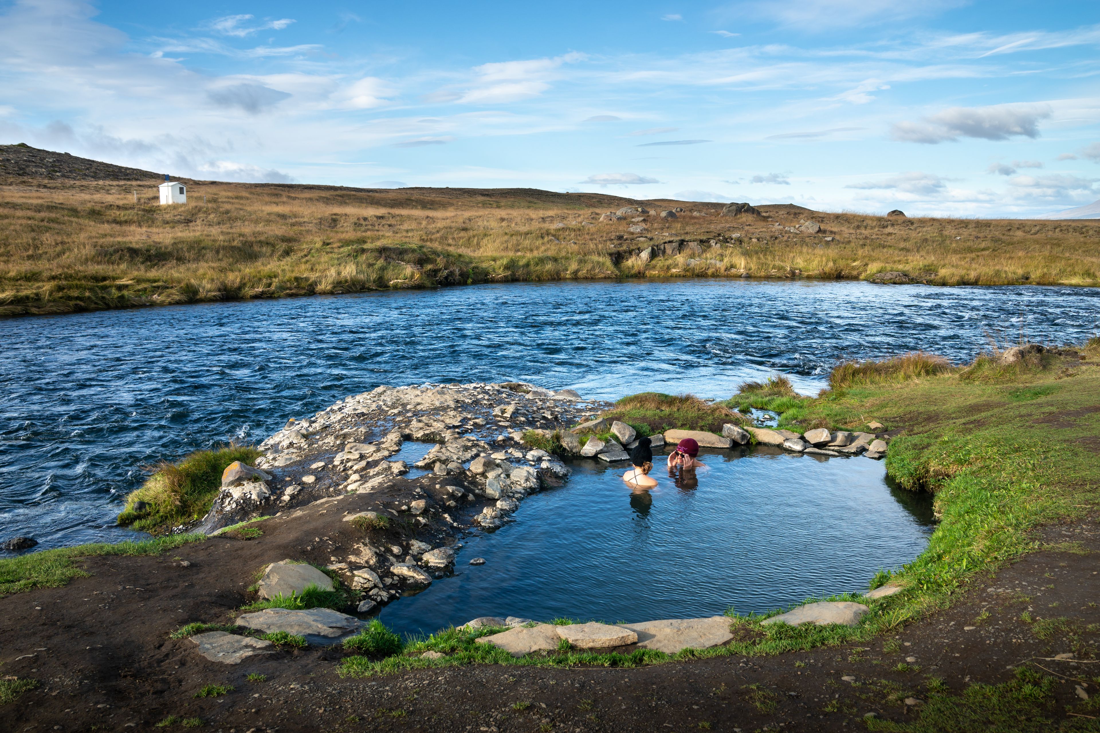 Two people inside Fosslaug hot springs, near a river