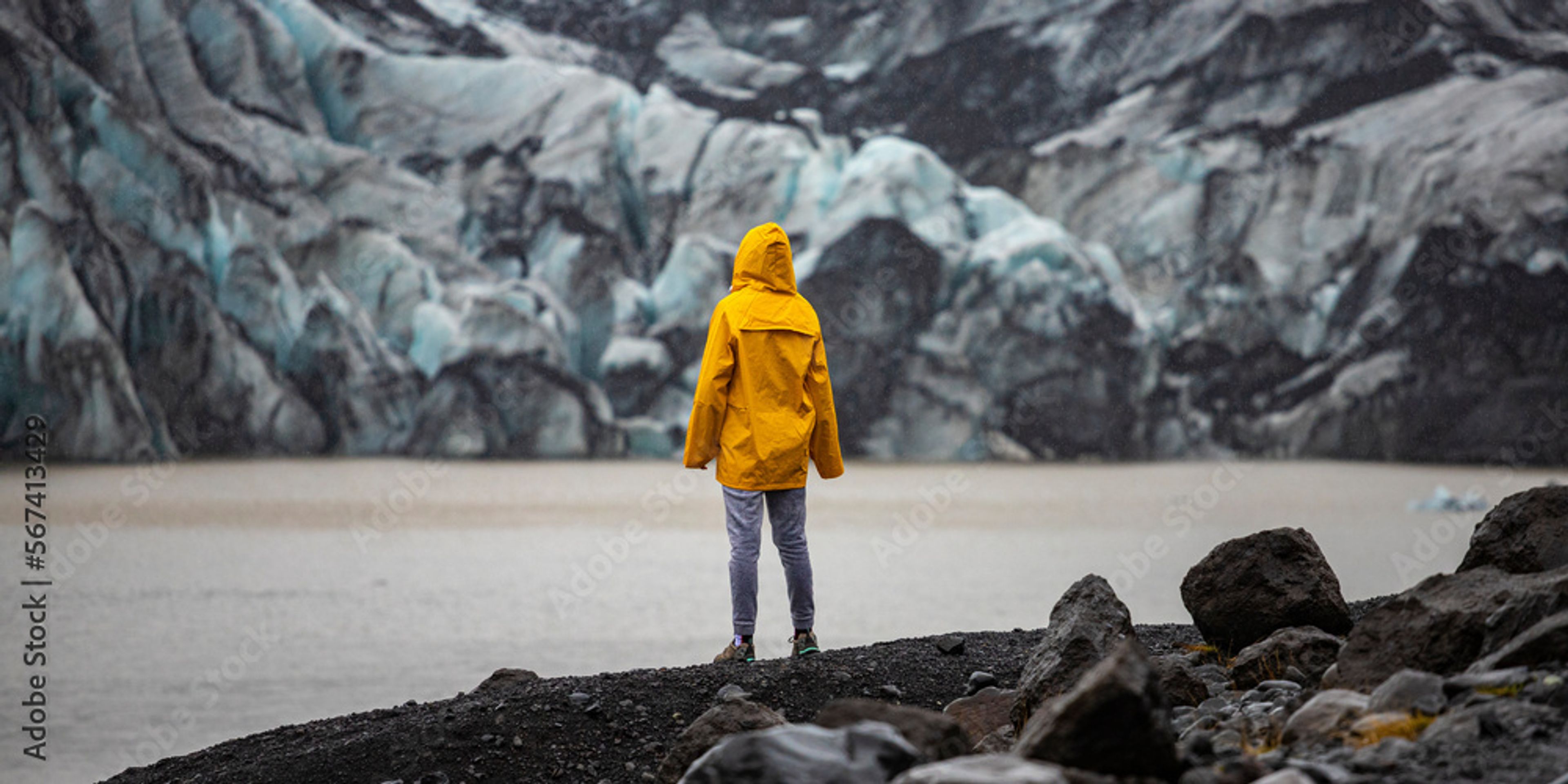 girl in a yellow raincoat admires the powerful big Katla glacier, Iceland