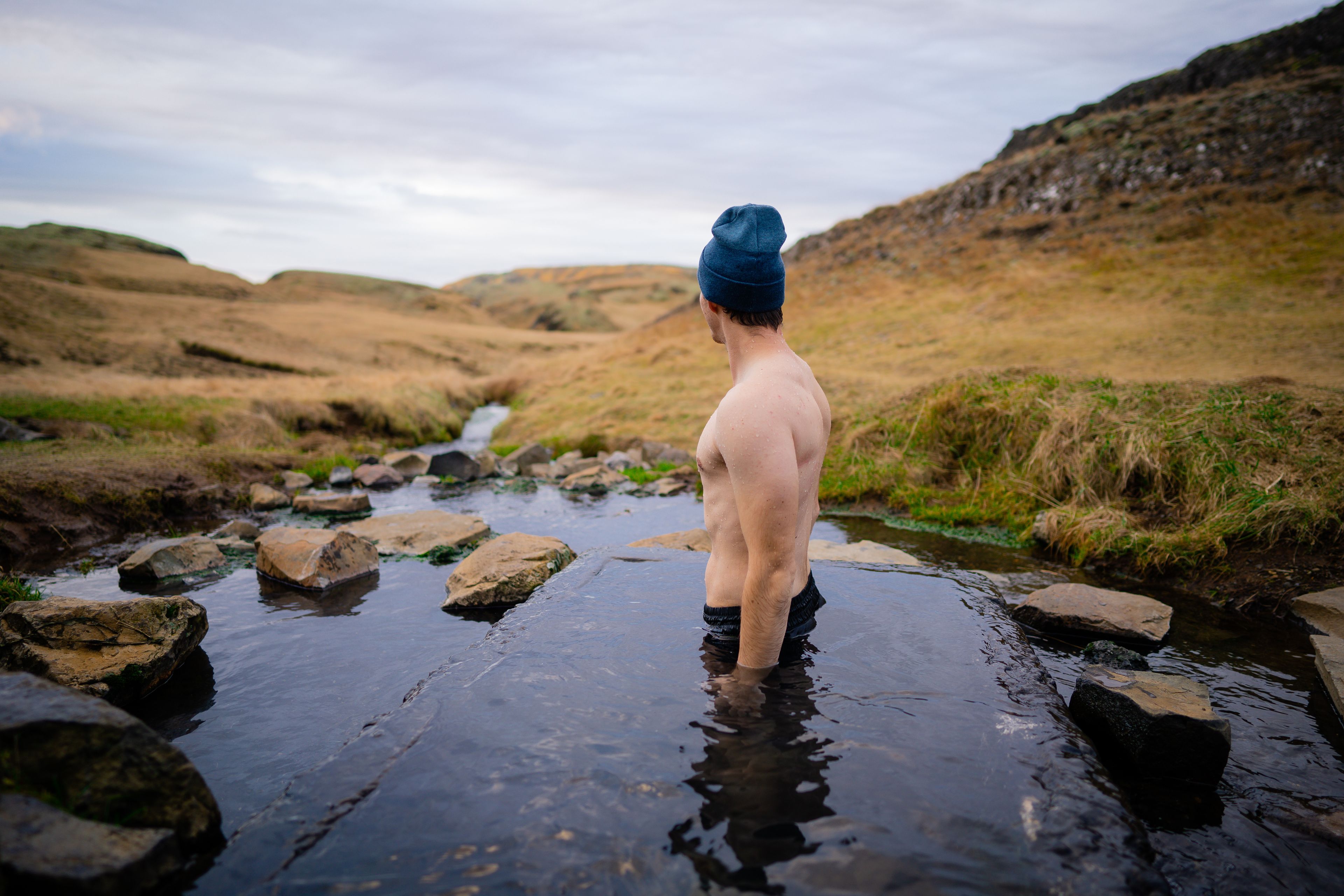 Man relaxing in a small geothermal hot spring pool in Hrunalaug, Iceland