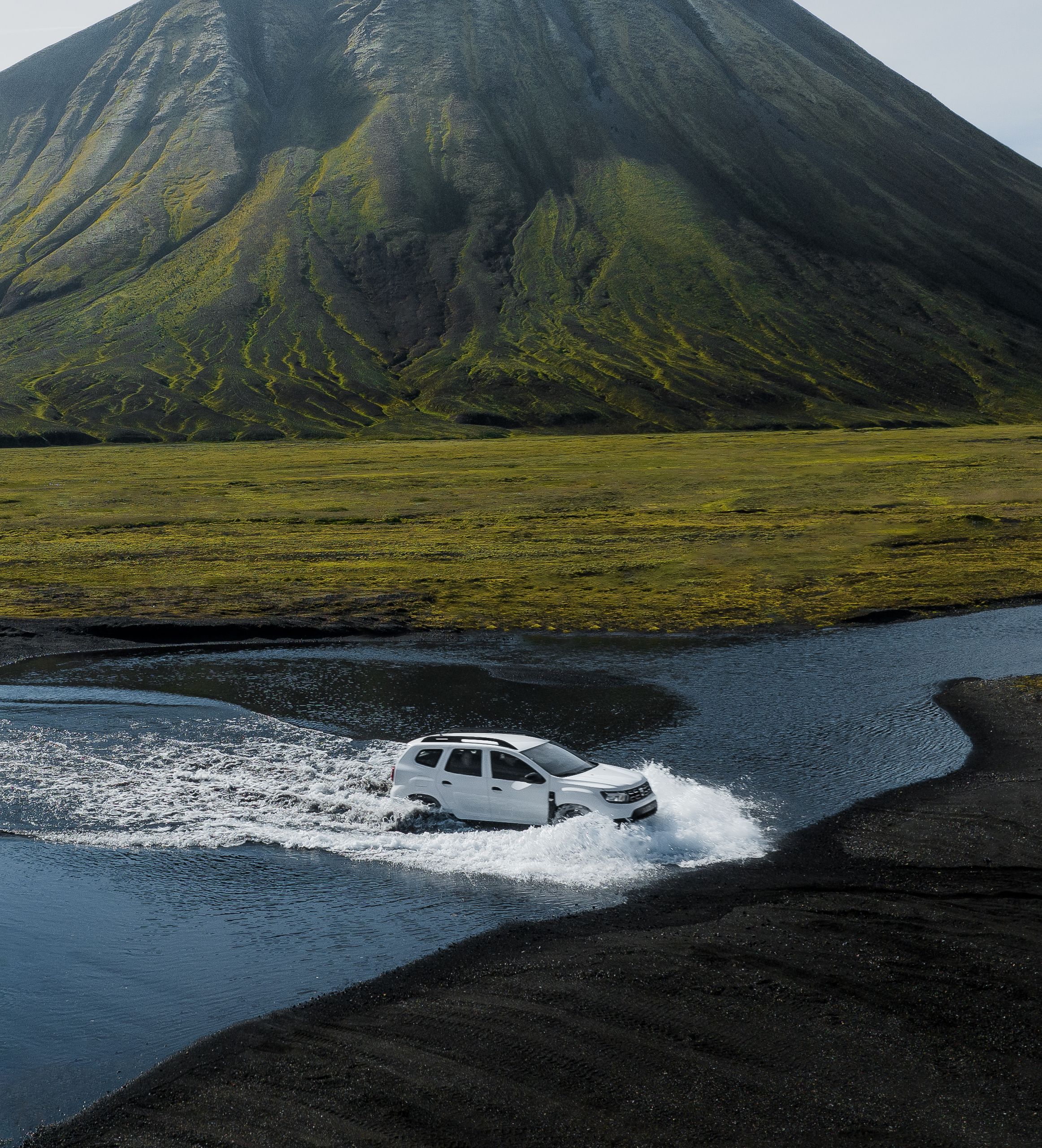 Dacia Duster SUV crossing a river in an F-road in Iceland surrounded by mountain