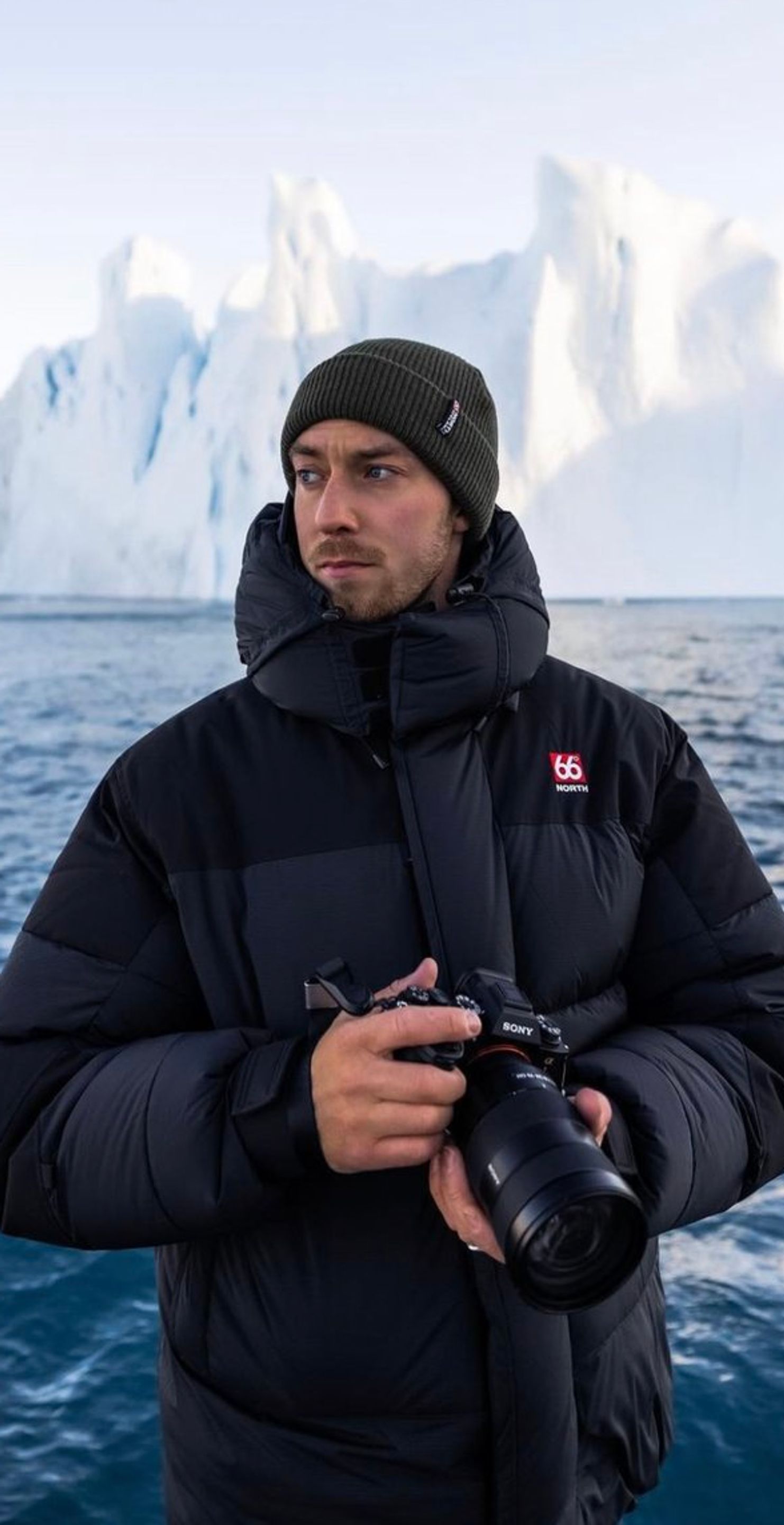 冰岛的Jón拿着相机，站在冰岛周围蓝色水域和冰山附近。