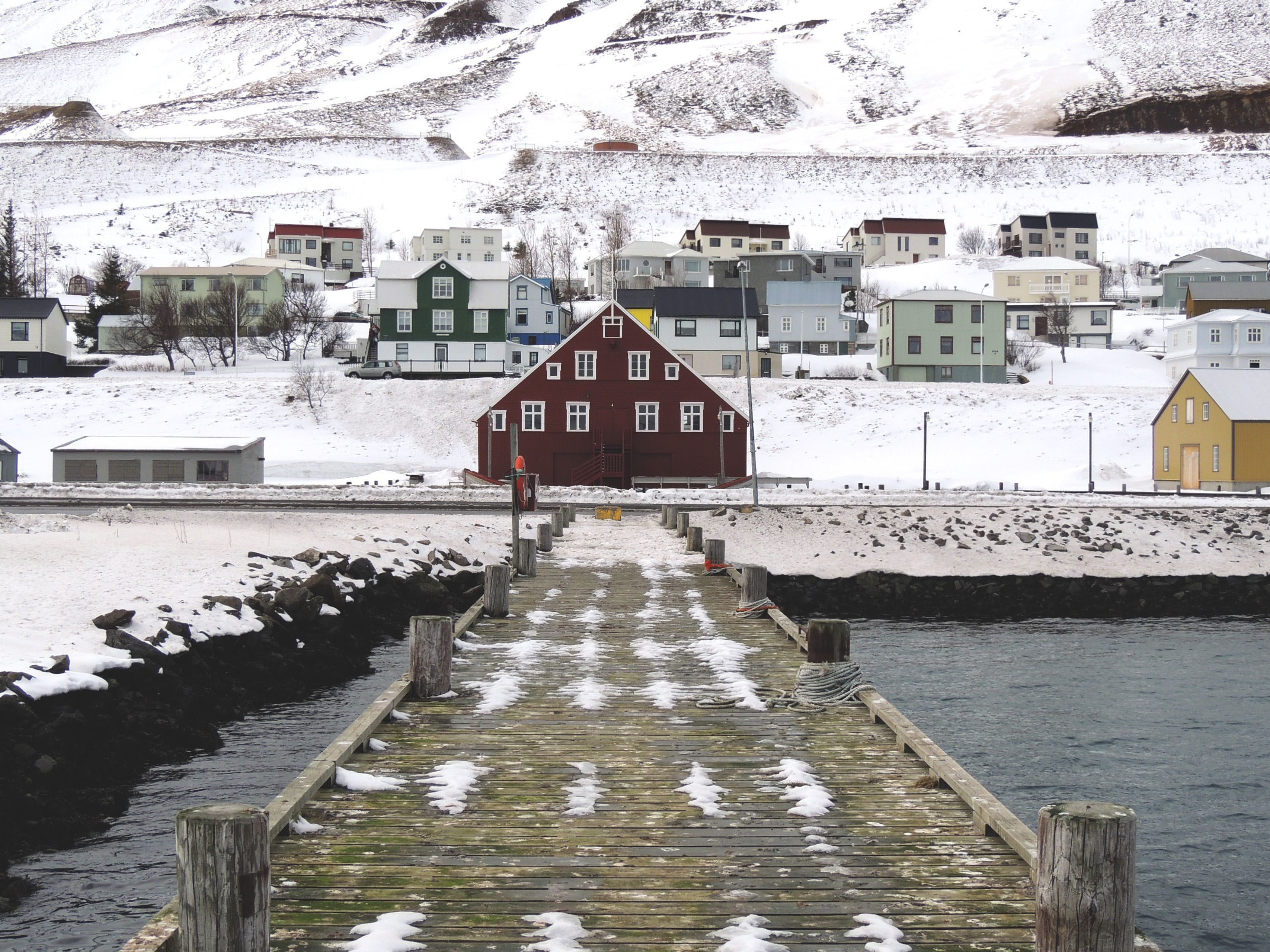 view on a pontoon and a snow-covered red house in the town of Siglufjörður in northern Iceland