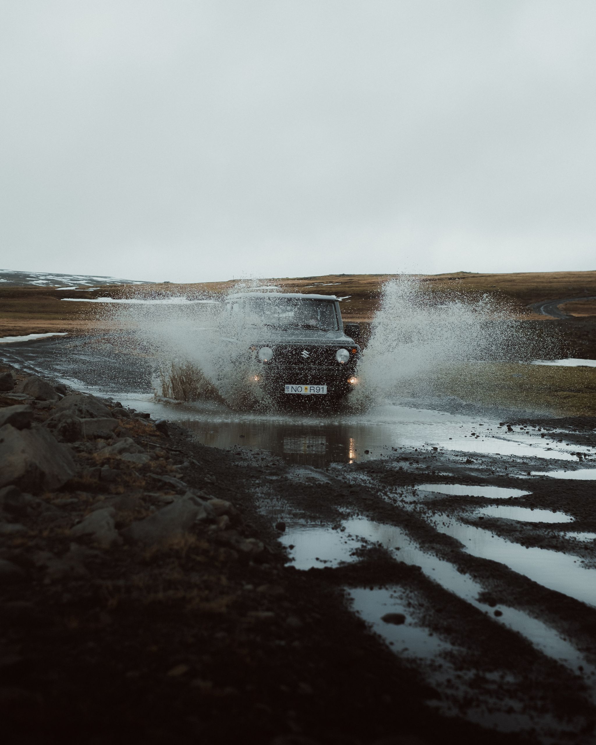A compact size Suzuki Jimny  rental vehicle dynamically splashing through a puddle on iceland's f roads (highlands)