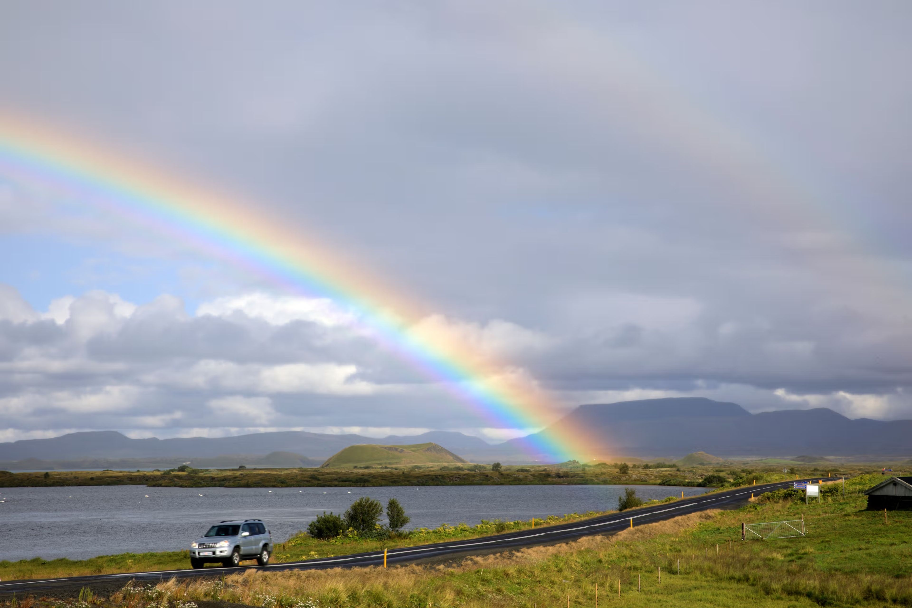 Car in a road in Iceland with a lake and a rainbow in the background