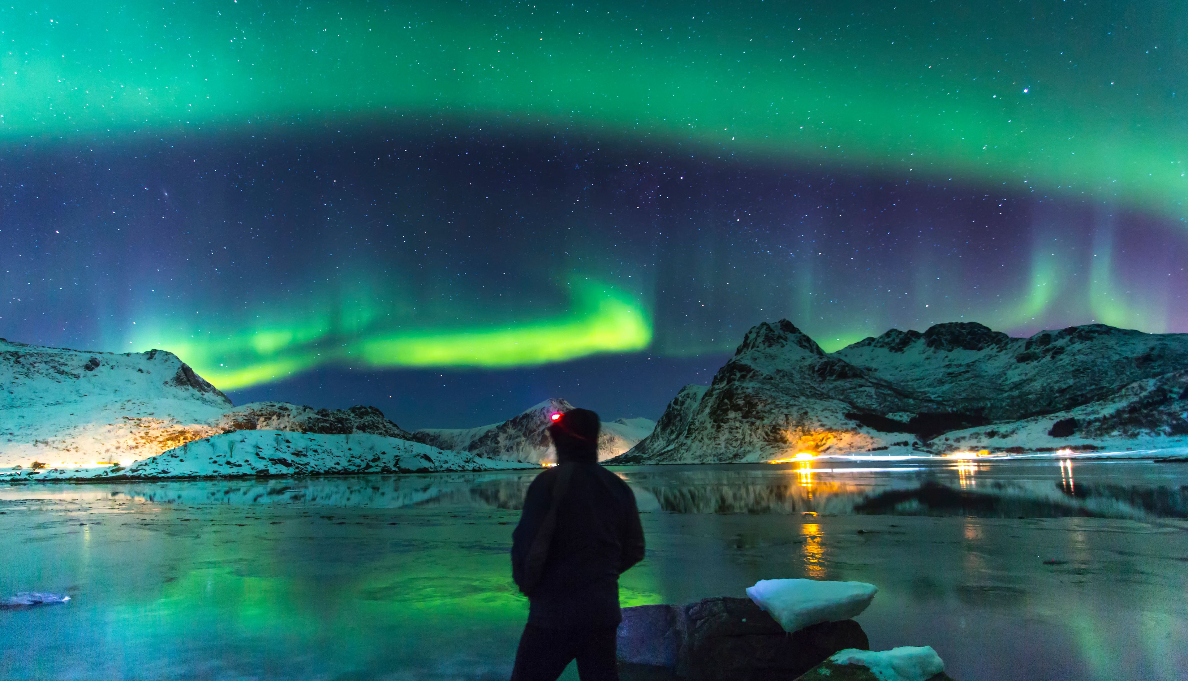 Exceptional view of a starry sky and aurora borealis in a winter landscape with snow-capped mountains. In the foreground a man alone admiring this spectacle