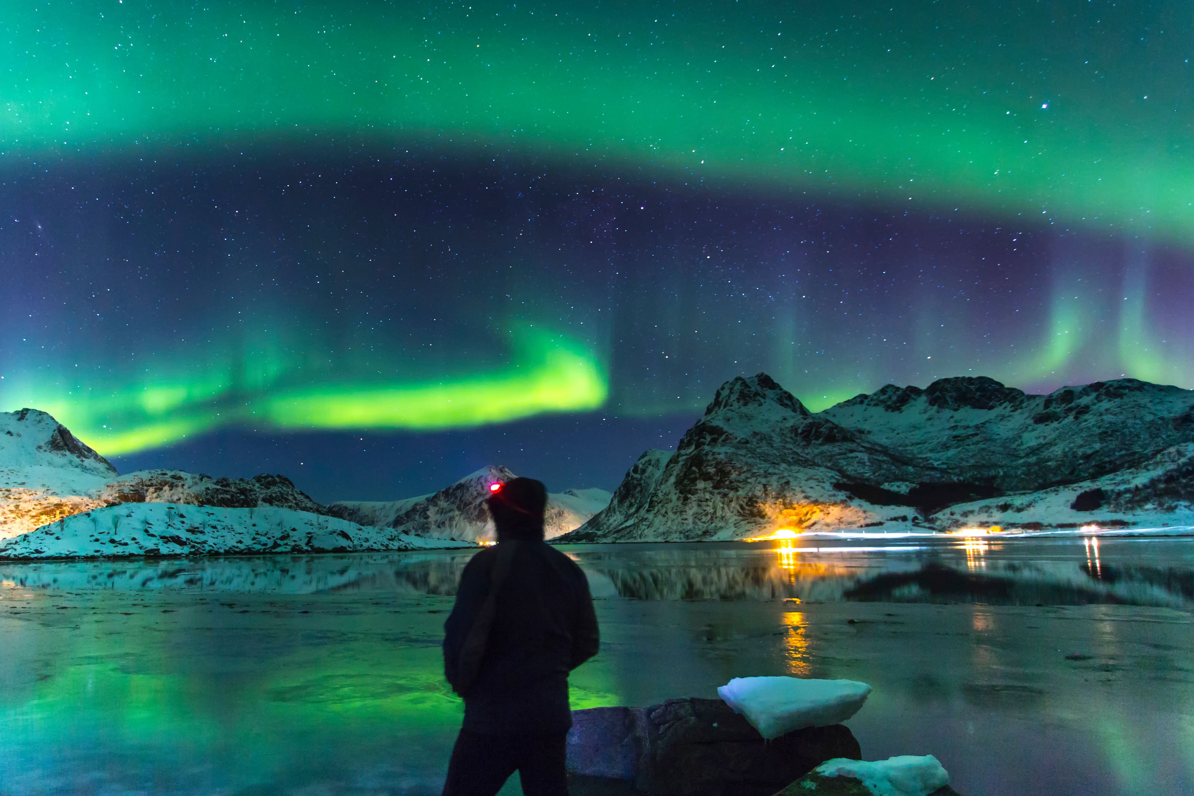 Exceptional view of a starry sky and aurora borealis in a winter landscape with snow-capped mountains. In the foreground a man alone admiring this spectacle