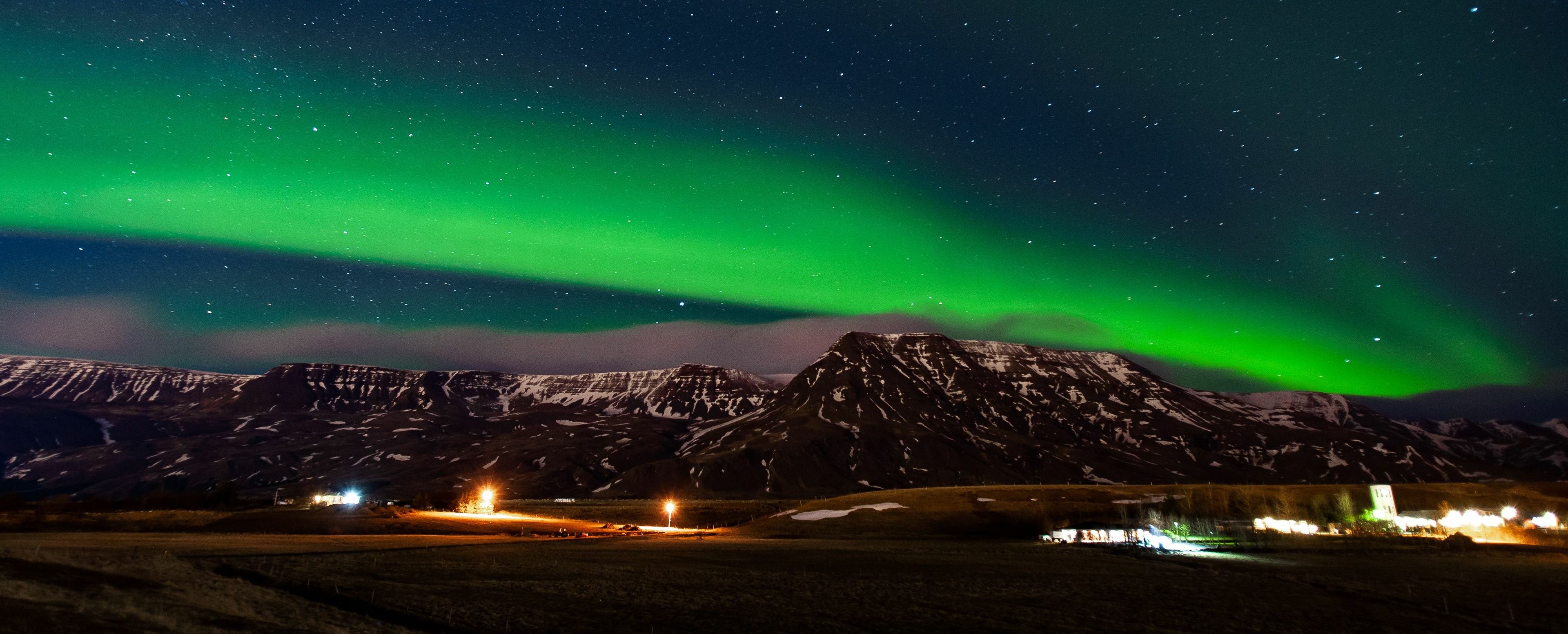 Northern lights with blue and starry sky in the countryside, snowy mountains in the background 
