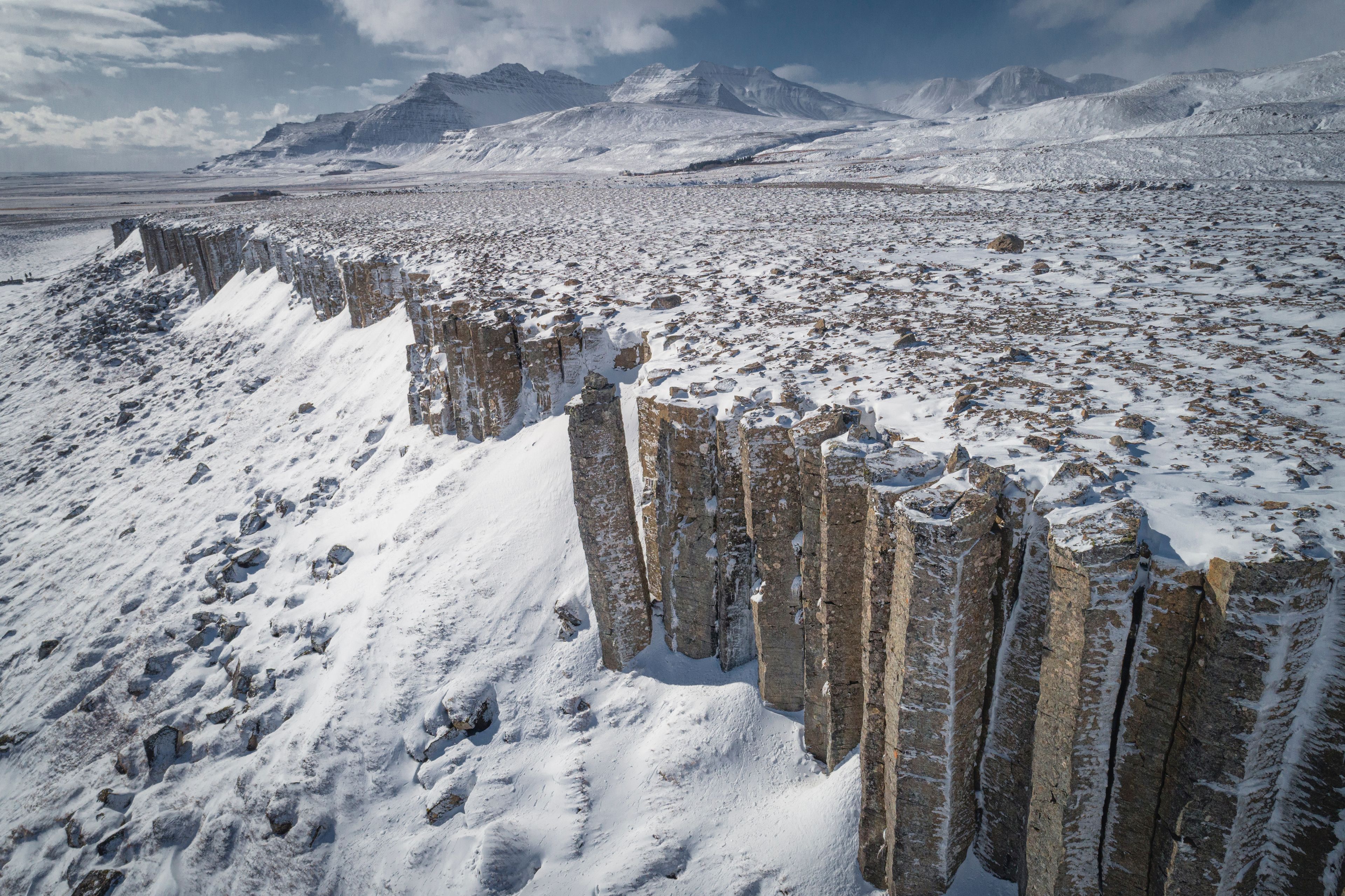 Hexagonal basalt columns at Gerðuberg cliffs with snow blanketed landscapes in the background