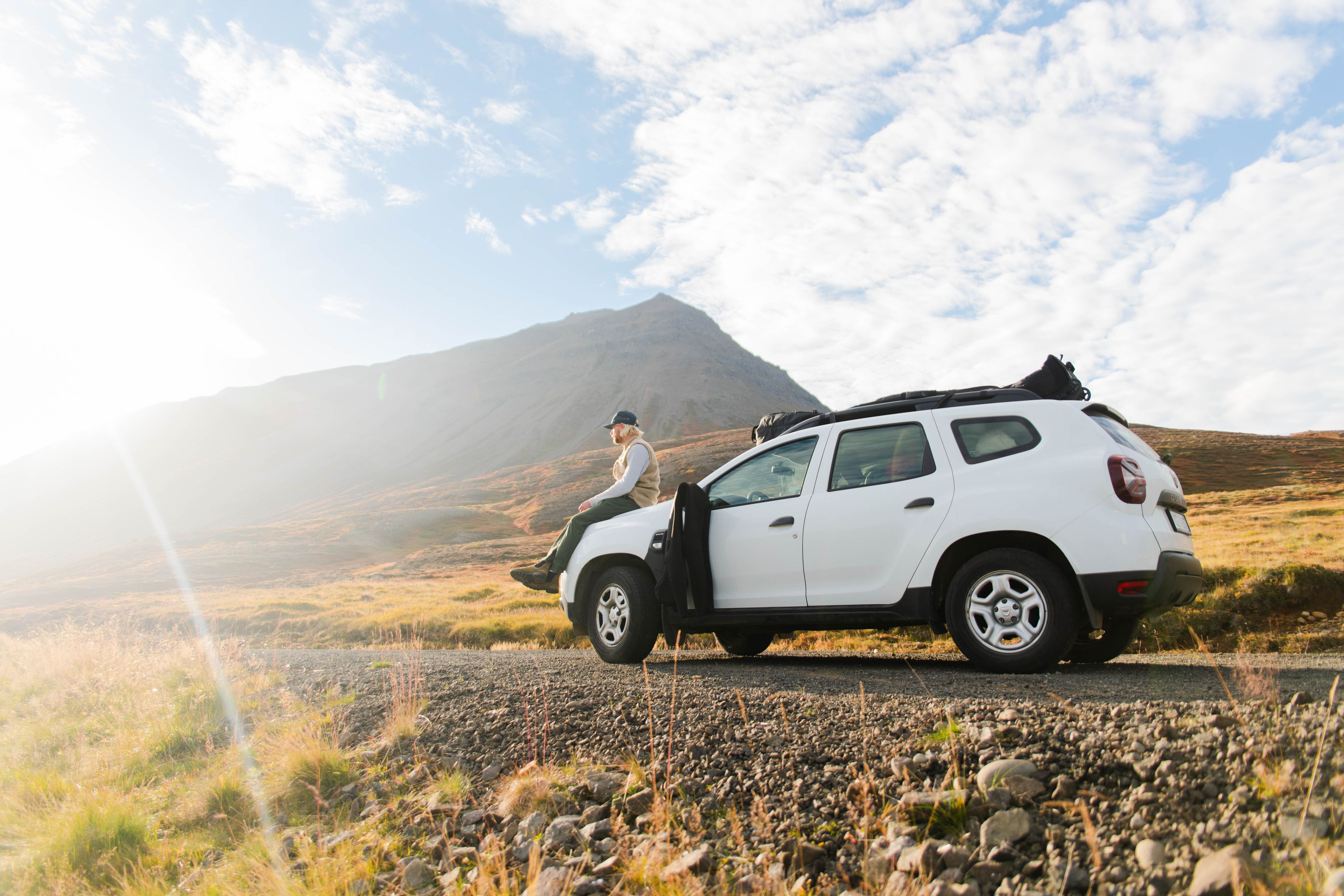 A man sitting on his white dacia duster rental car with the sun in his face